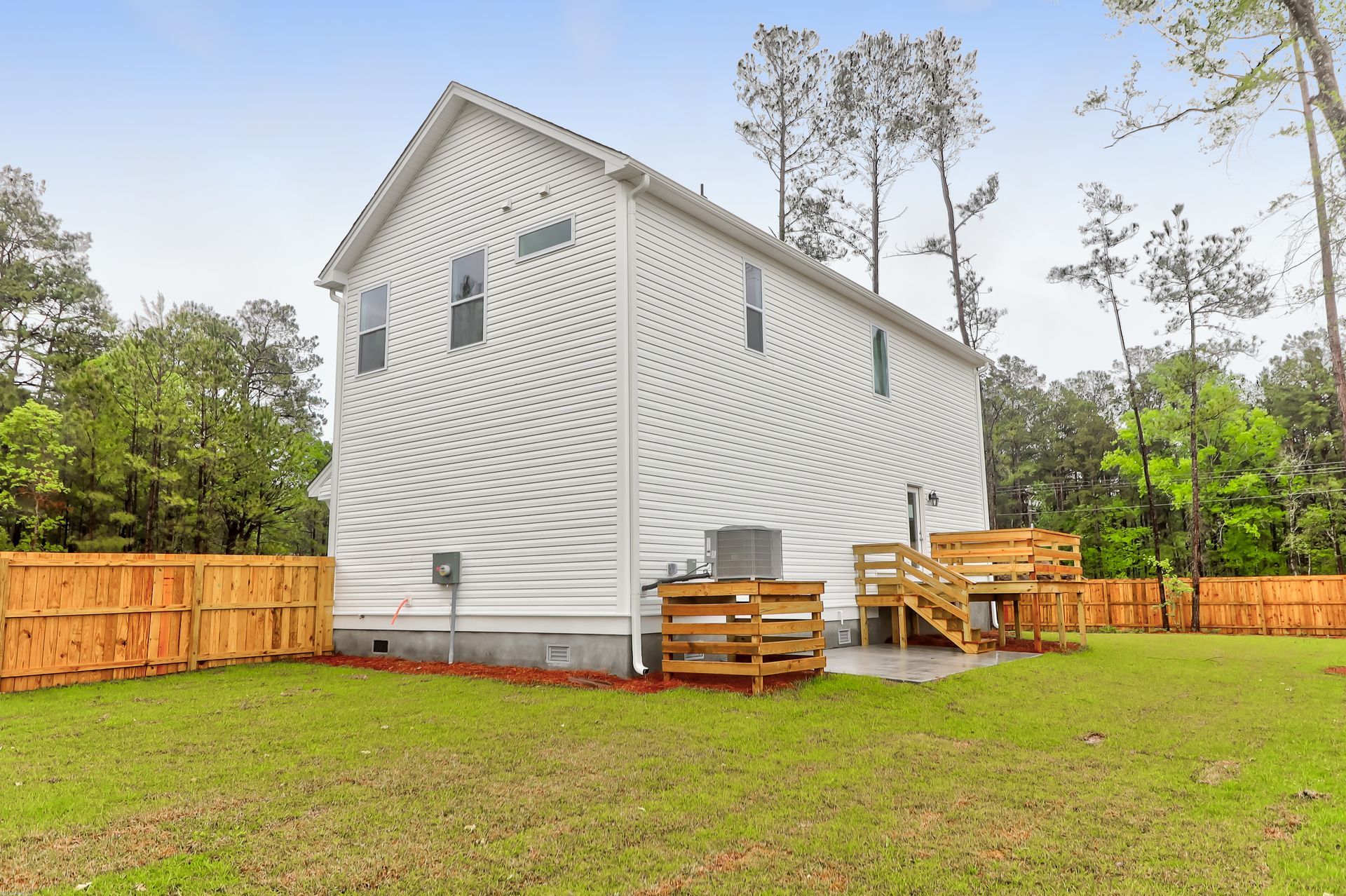 A white house with a wooden deck in the backyard surrounded by trees.