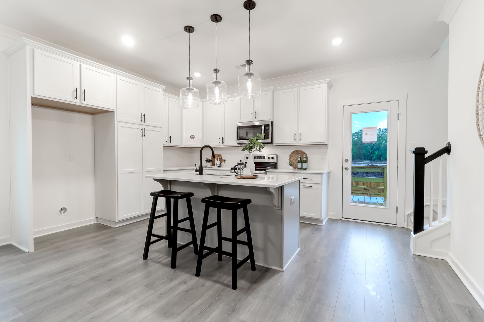 A kitchen with white cabinets , black stools and a large island.