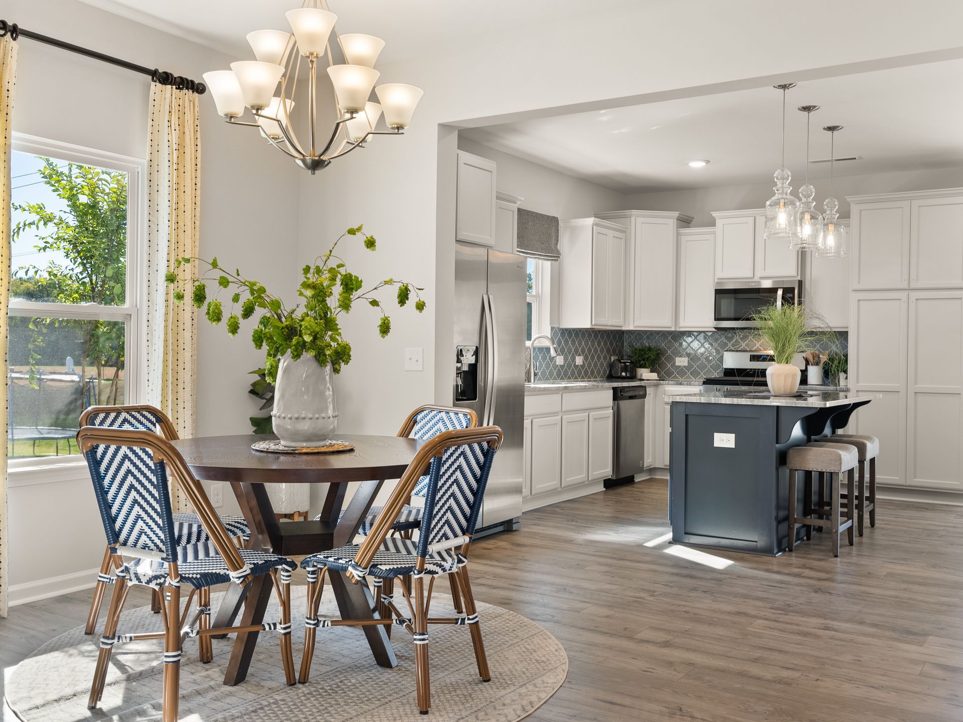 A dining room with a table and chairs and a kitchen in the background.