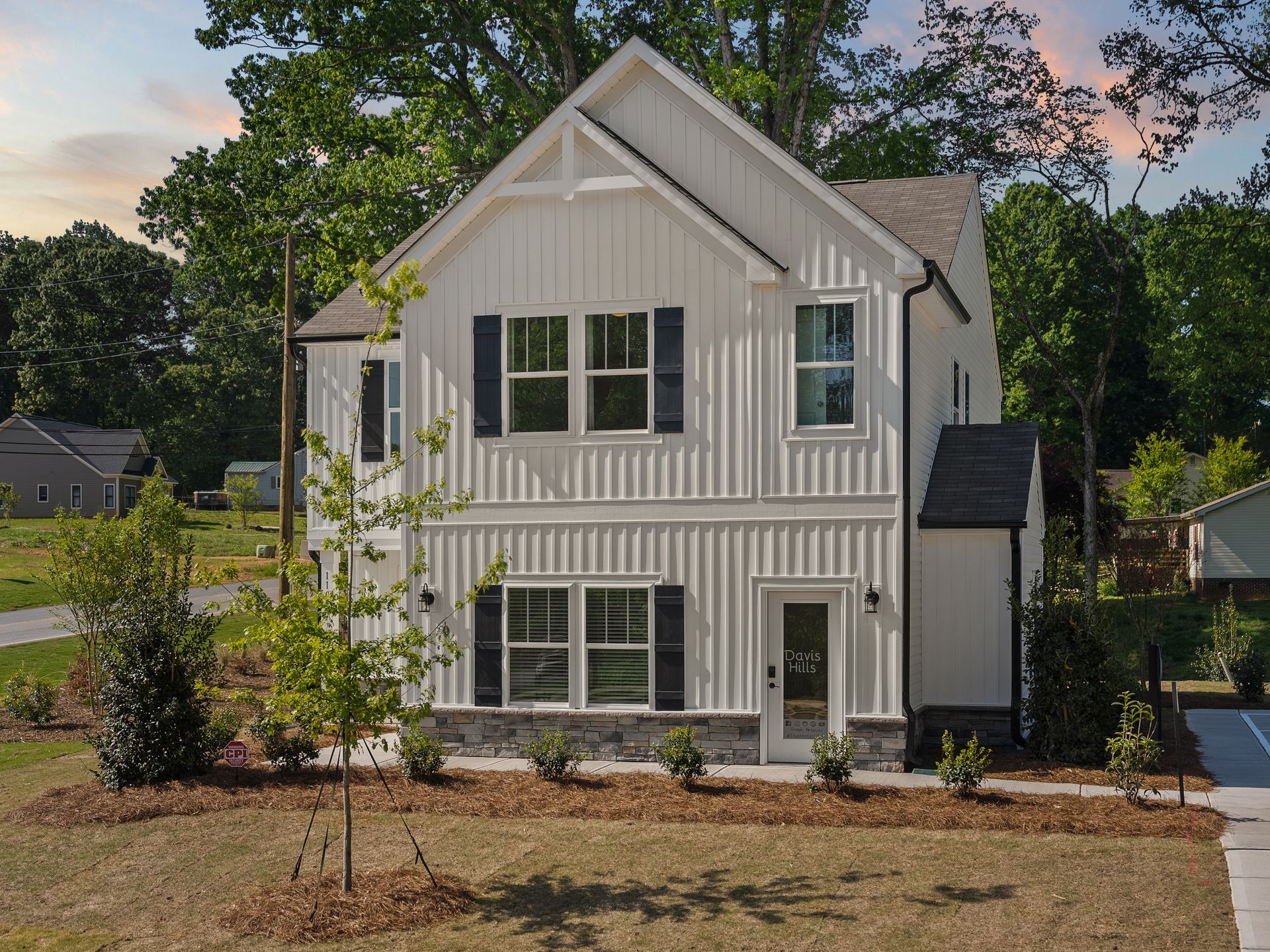 A white house with black shutters is surrounded by trees and grass.