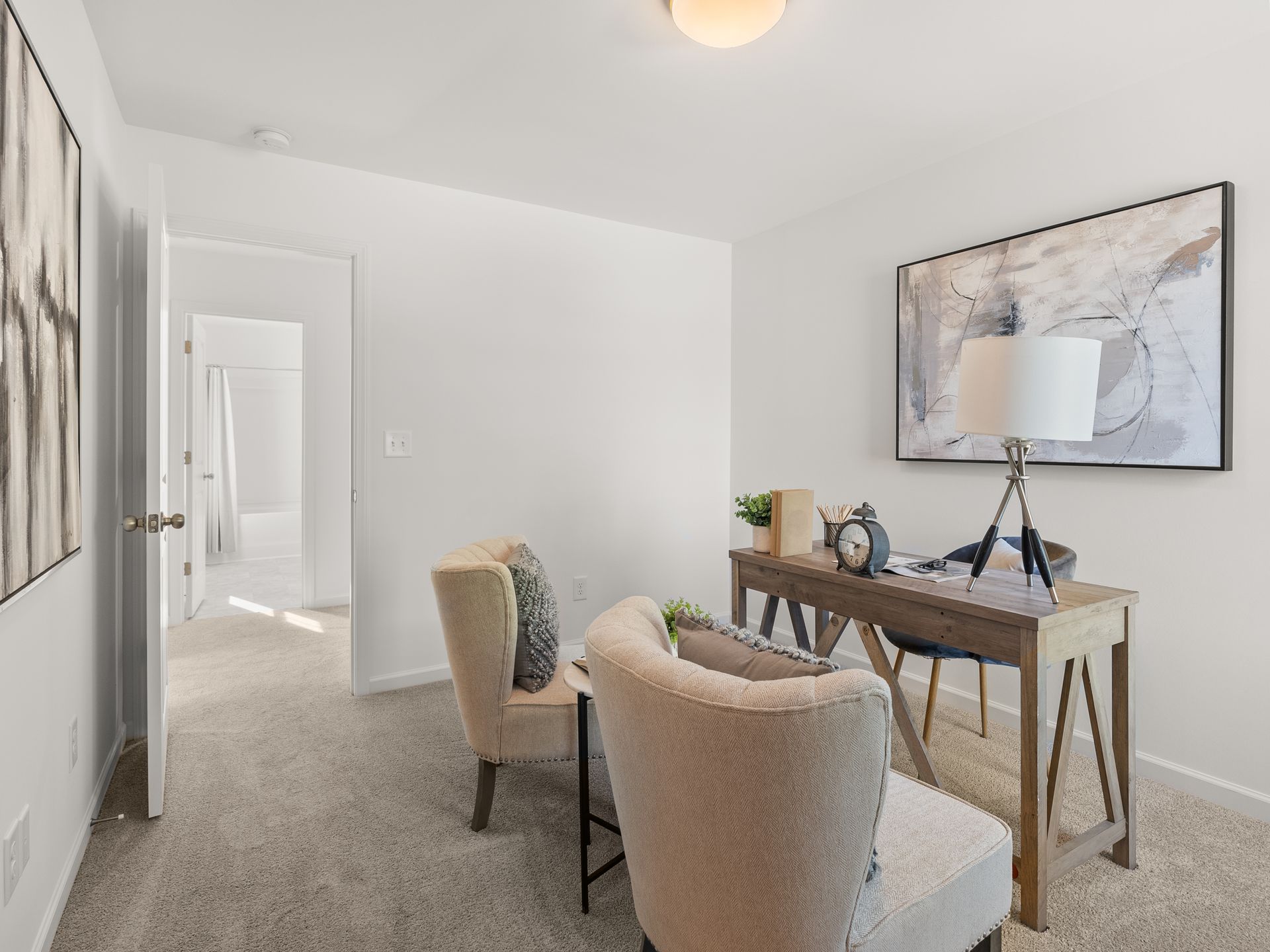 A home office with a desk , chairs and a painting on the wall.