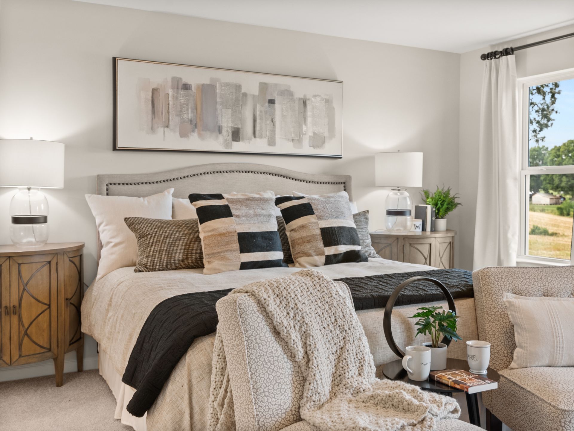 A bedroom with a bed , chair , nightstand , lamps and a window.