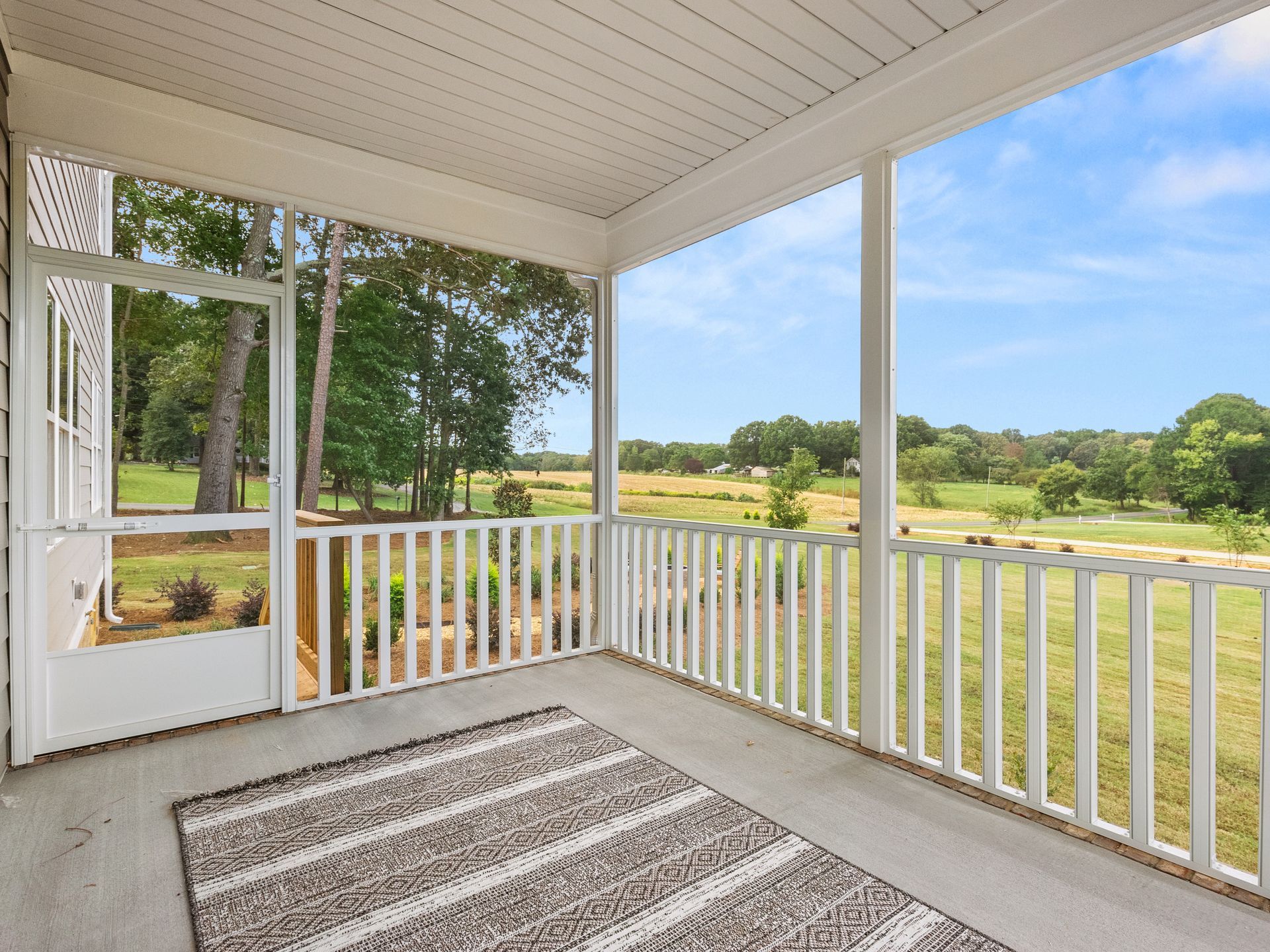 A screened in porch with a rug and a view of a field.