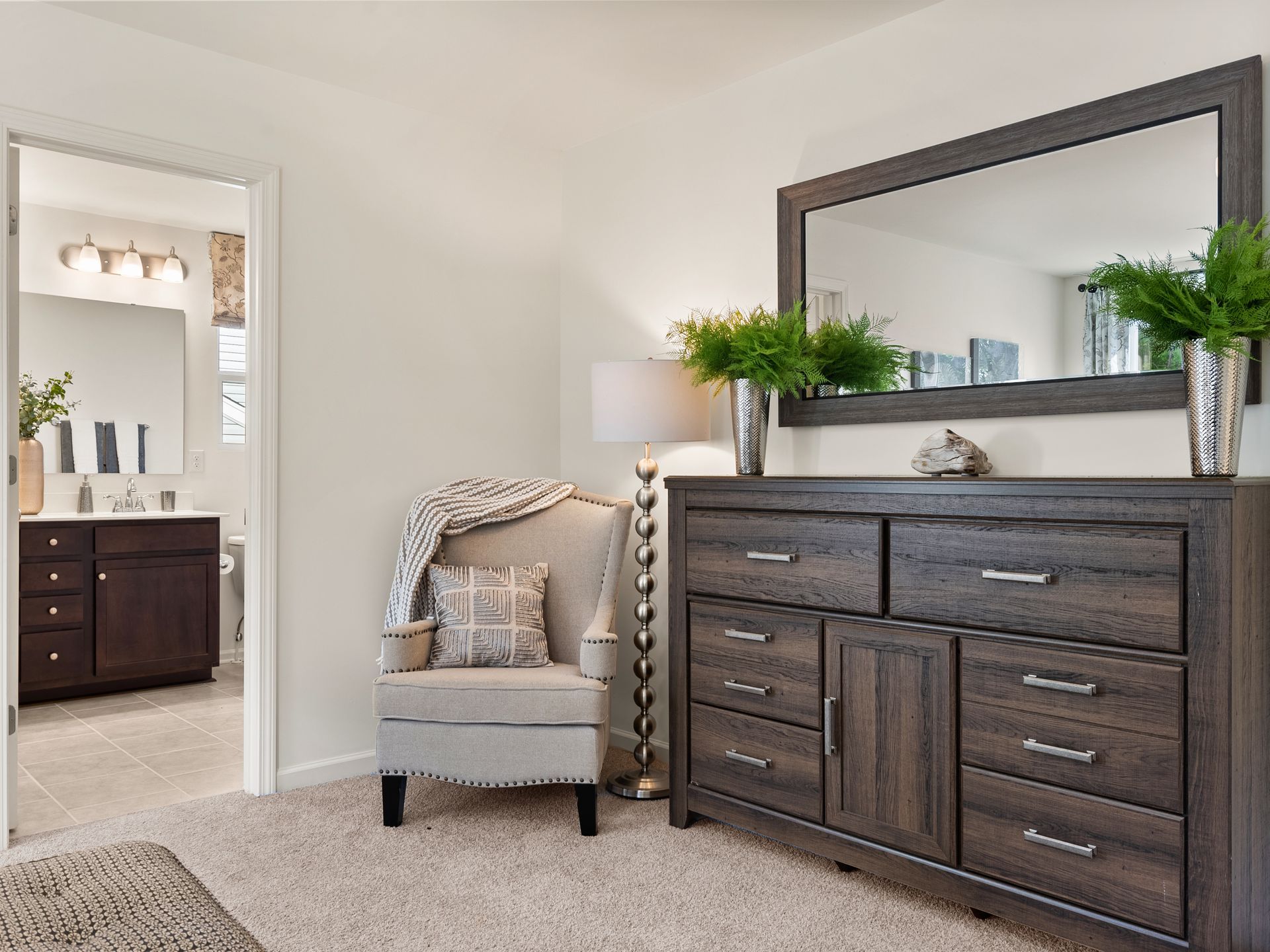 A bedroom with a chair , dresser and mirror.