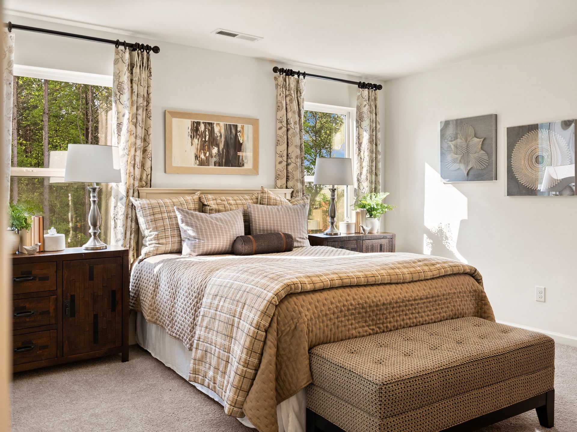 A bedroom with a bed , nightstand , ottoman , and two windows.