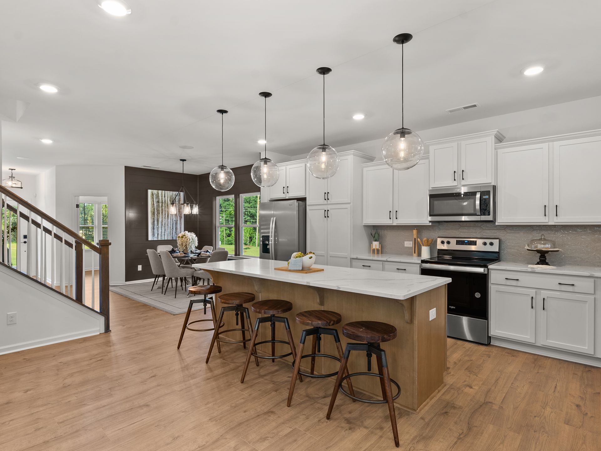 A kitchen with white cabinets , stainless steel appliances , a large island and stools.