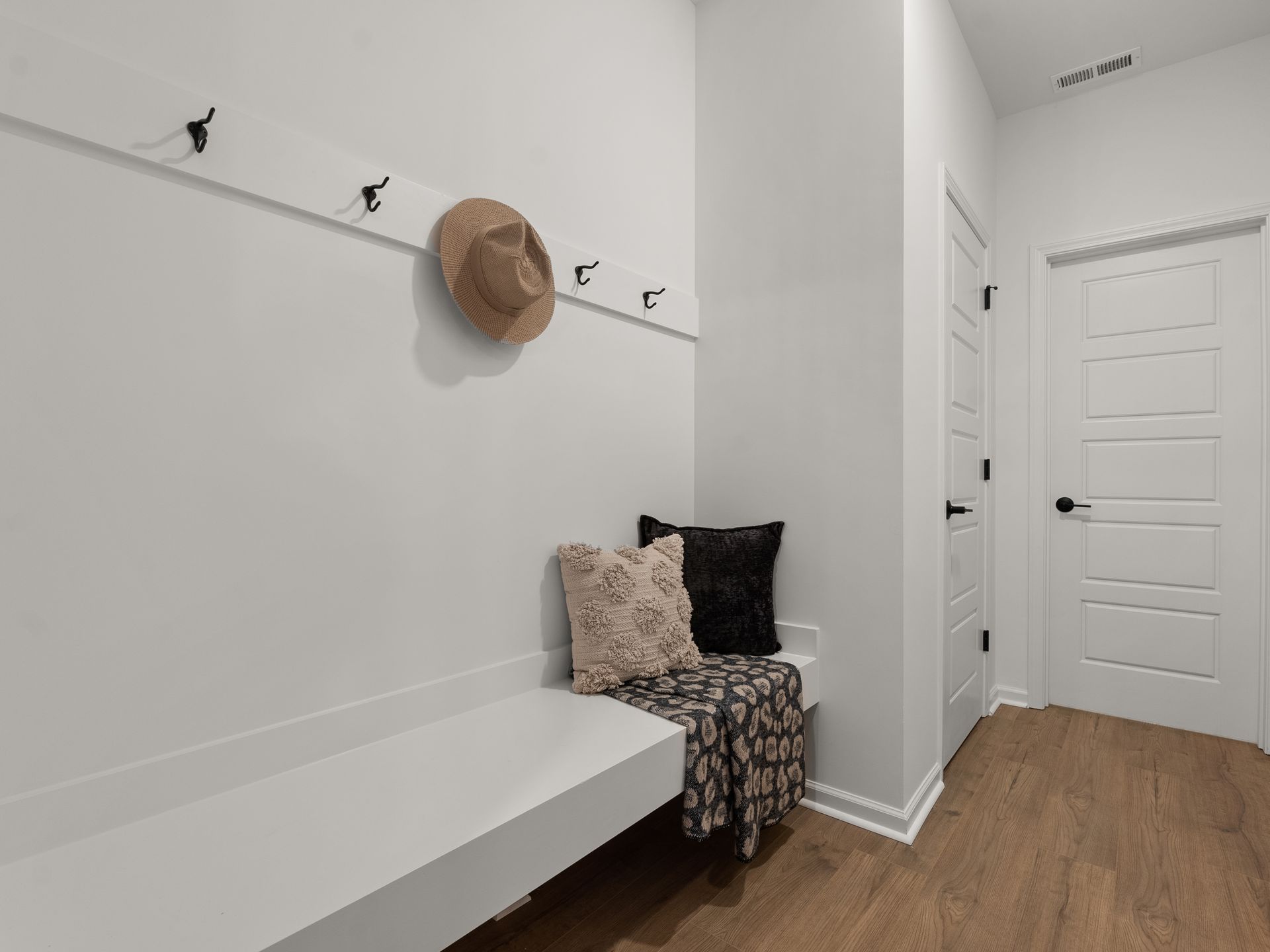 There is a bench in the hallway with a hat hanging on the wall.