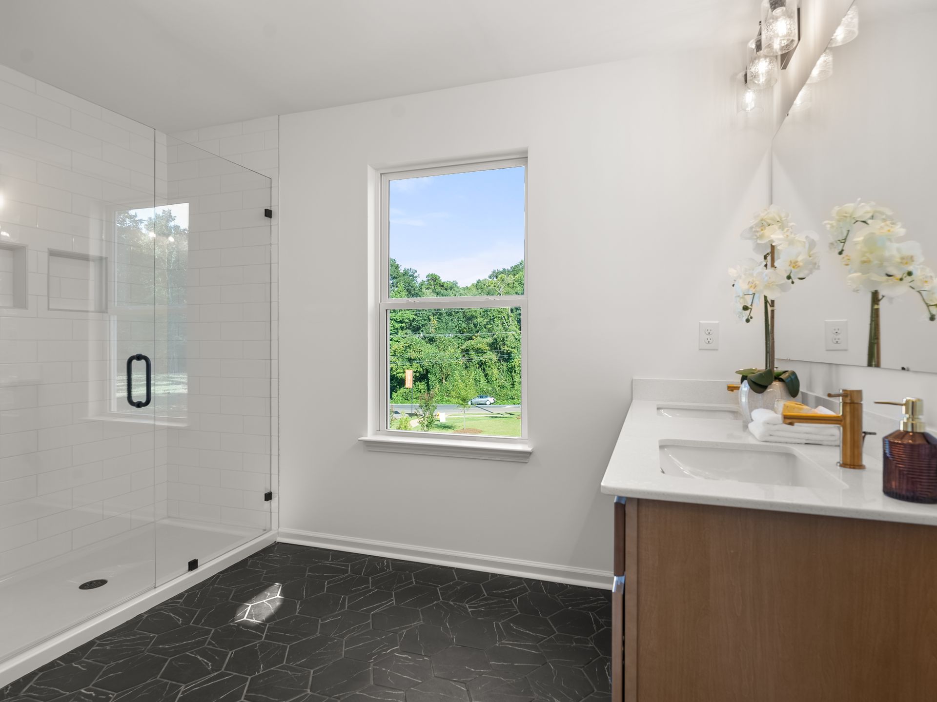 A bathroom with two sinks , a walk in shower and a window.