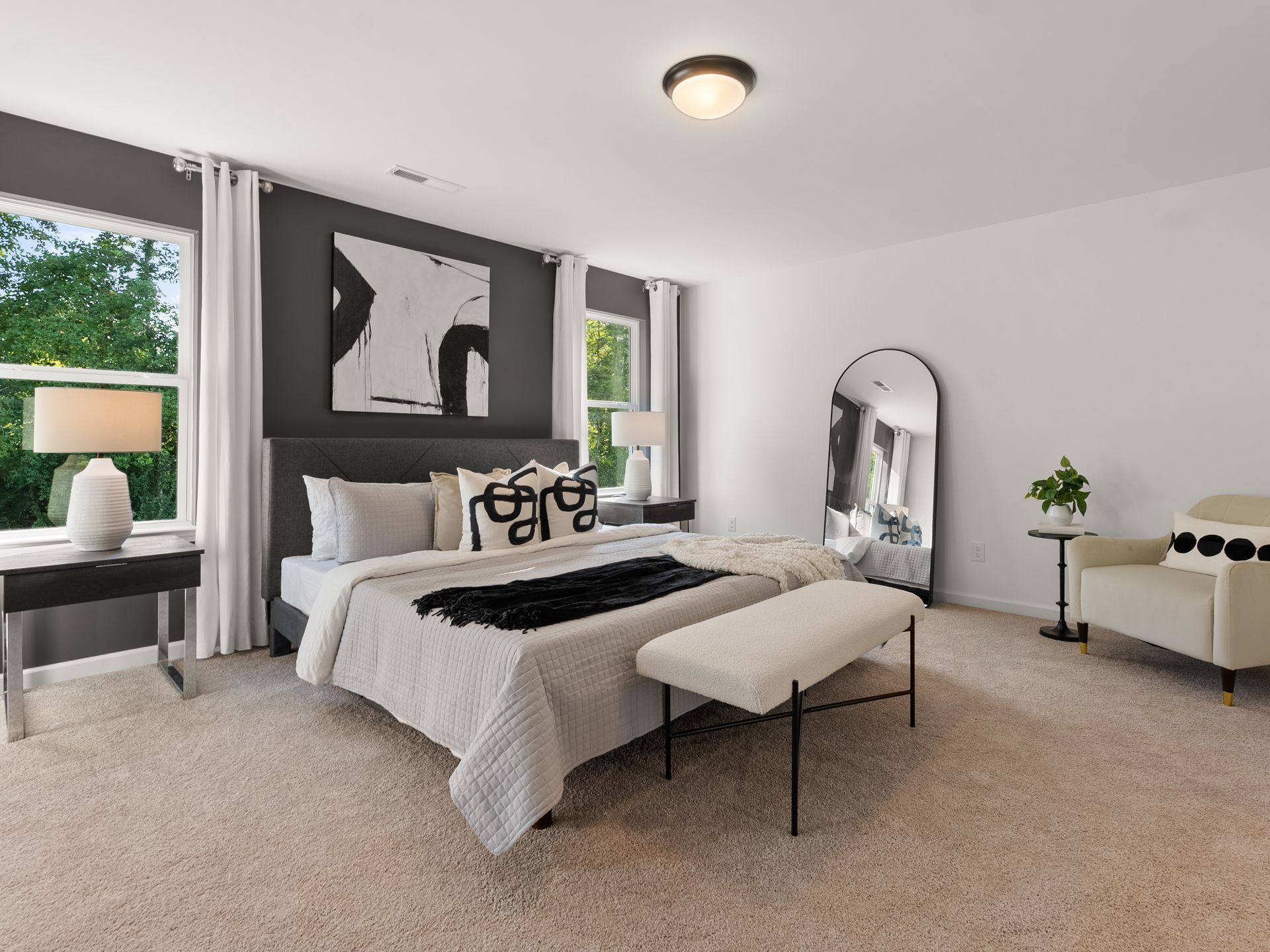 A bedroom with a large bed , chair , bench and mirror.