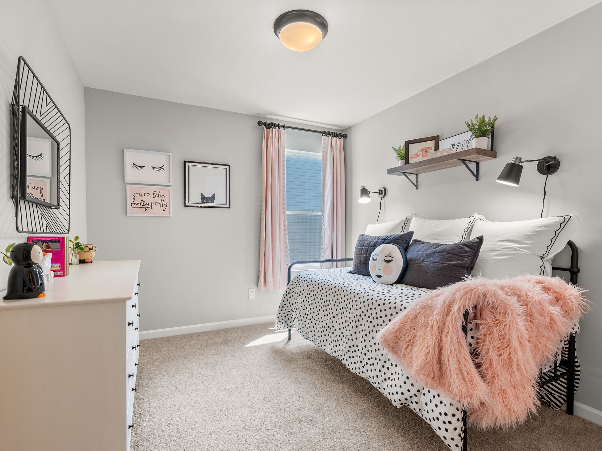 A bedroom with a day bed , dresser , mirror and window.