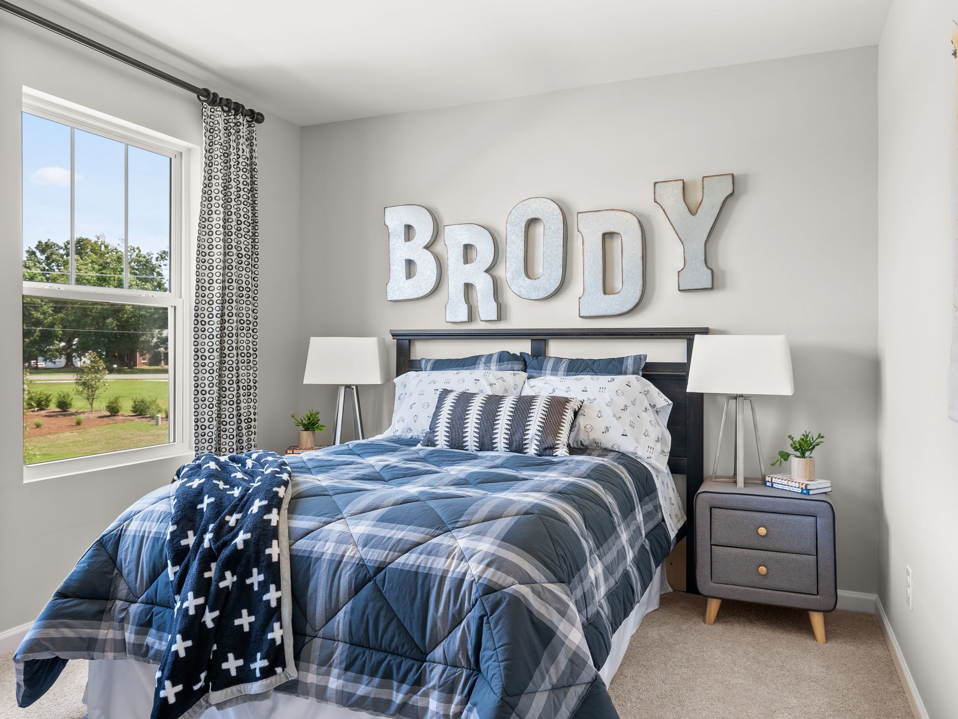A bedroom with a bed , nightstand , and window with the name brody on the wall.