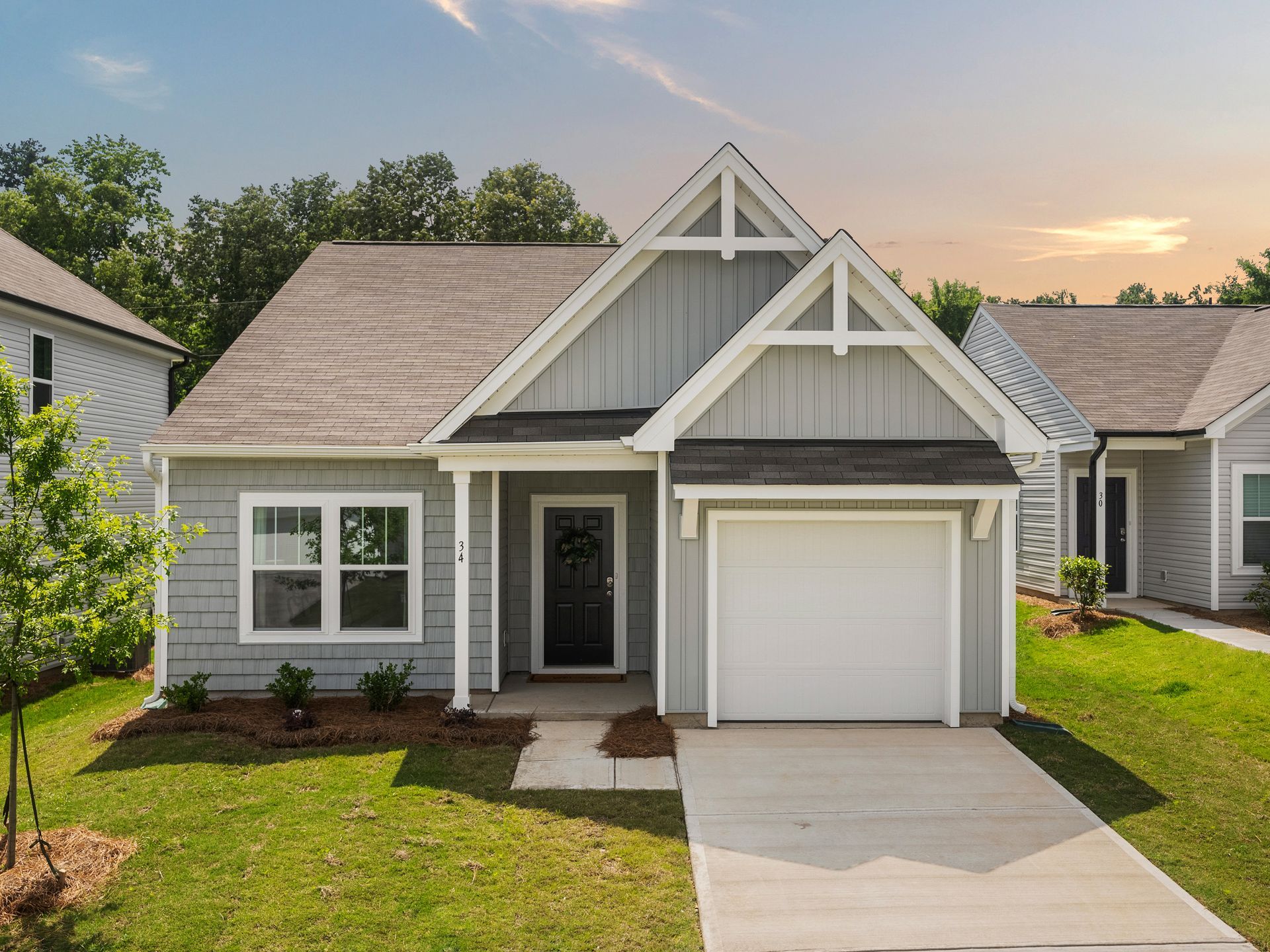 A small gray house with a white garage door is sitting on top of a lush green lawn.
