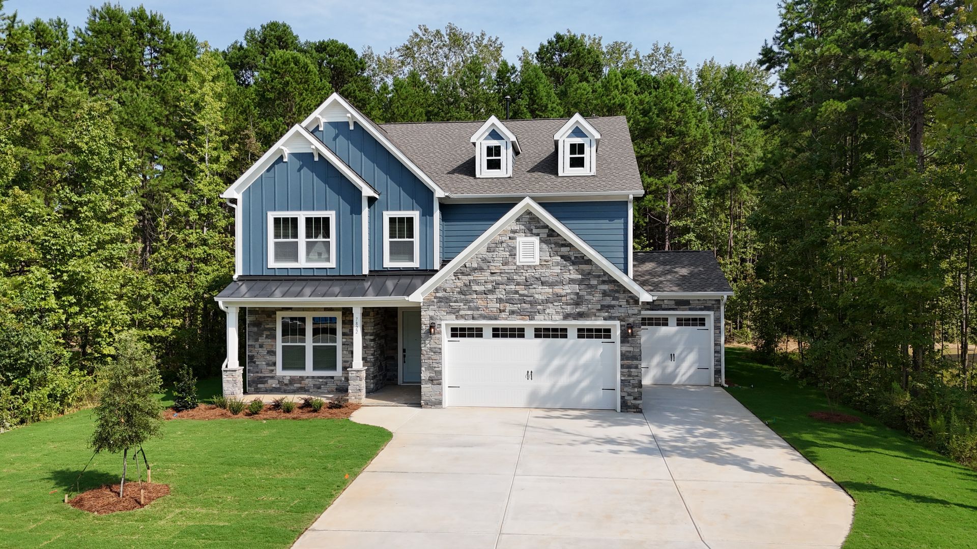 A blue and white house with a driveway and trees in the background