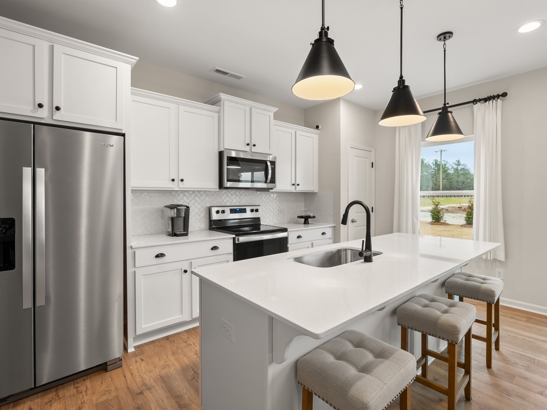 A kitchen with white cabinets , stainless steel appliances , a refrigerator and a sink.