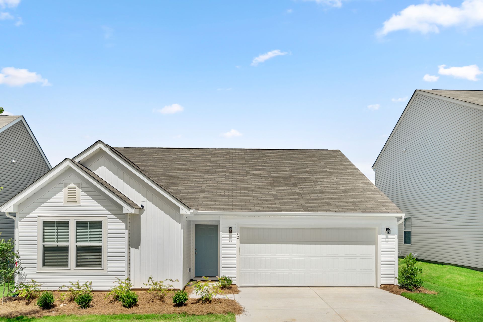 A white house with a brown roof and a white garage door is for sale.