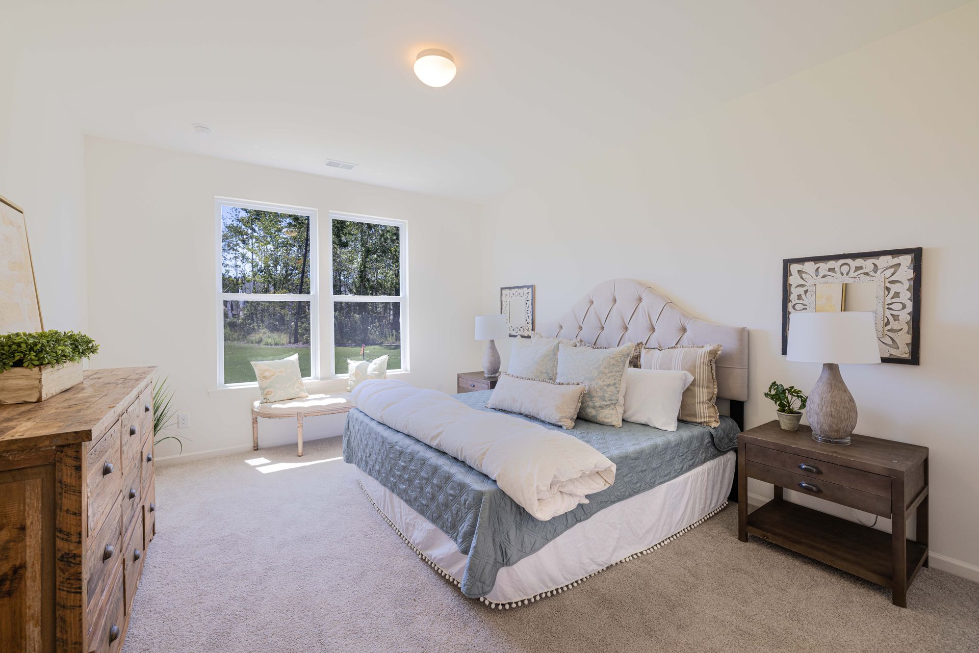 A bedroom with a bed , dresser , nightstand and two windows.