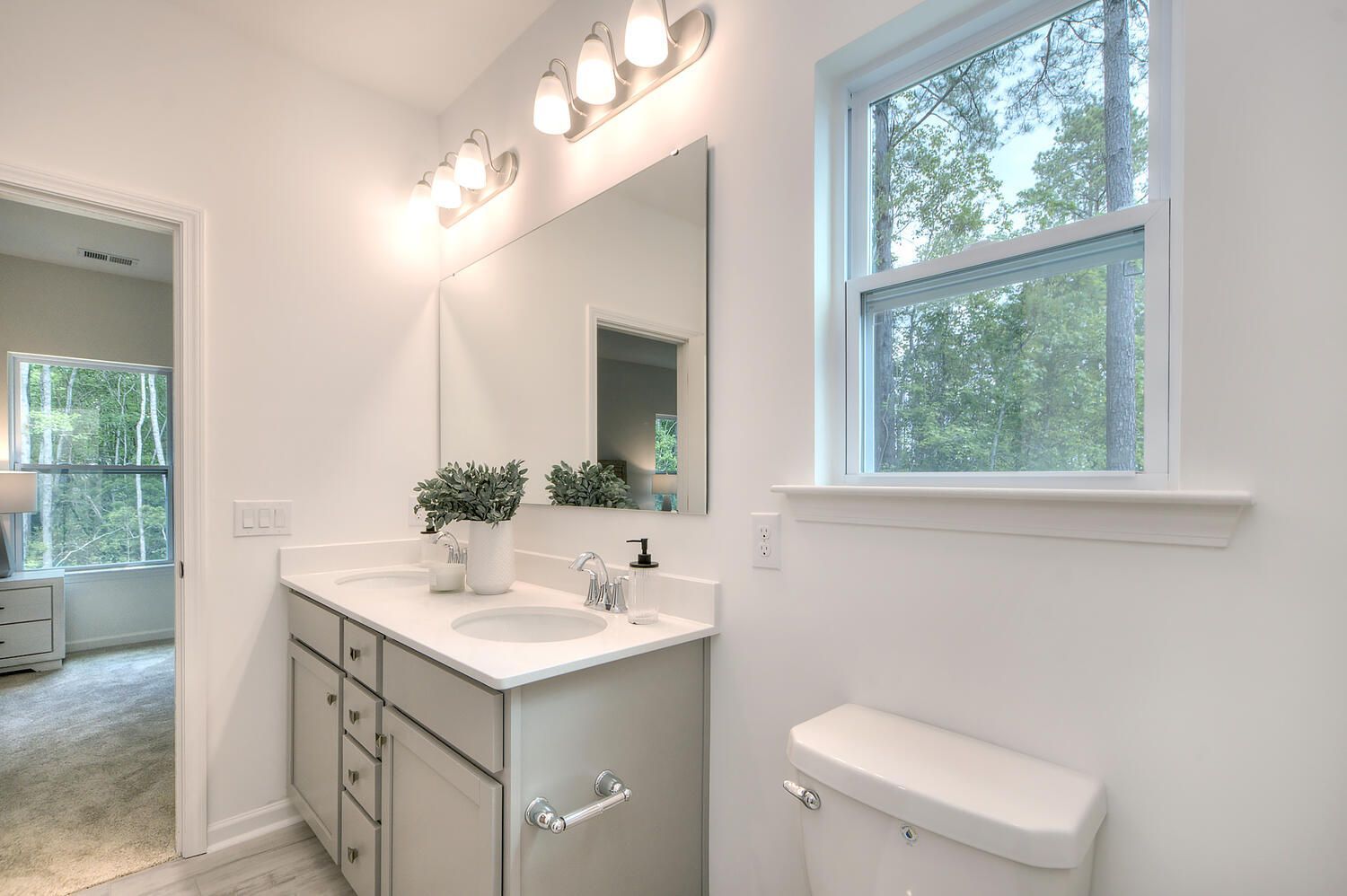 A bathroom with a toilet , sink , mirror and window.
