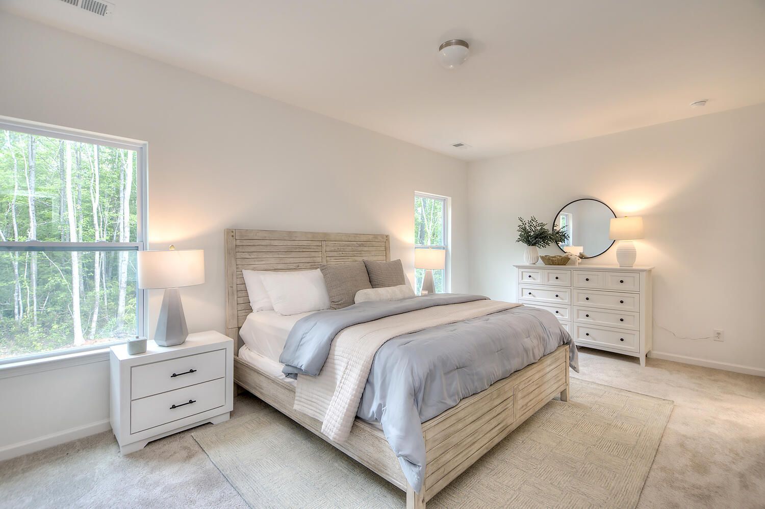 A bedroom with a bed , dresser , nightstand , mirror and two windows.