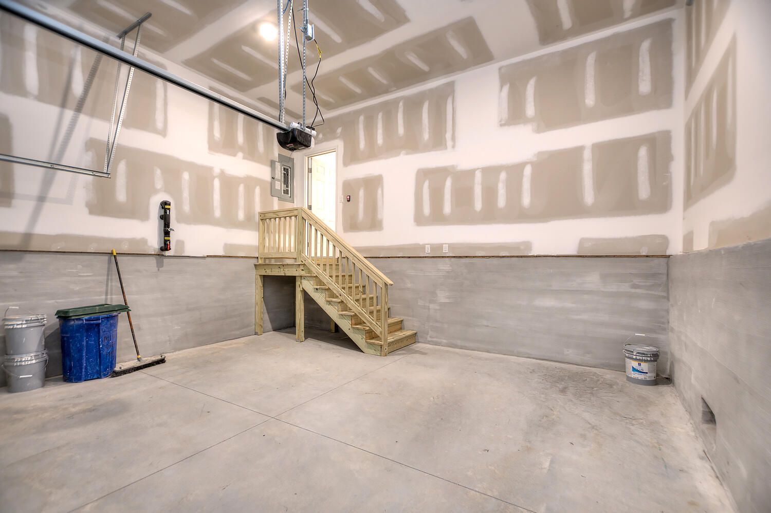 An empty garage with a wooden staircase and a garage door opener.