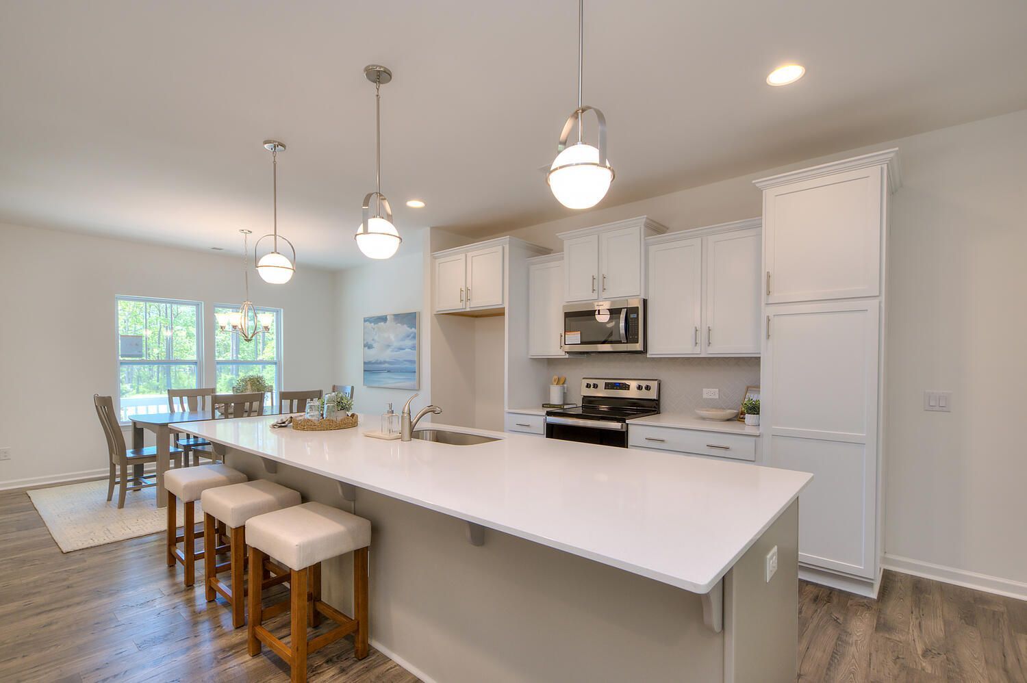 A kitchen with white cabinets , a large island , stools and a dining room.