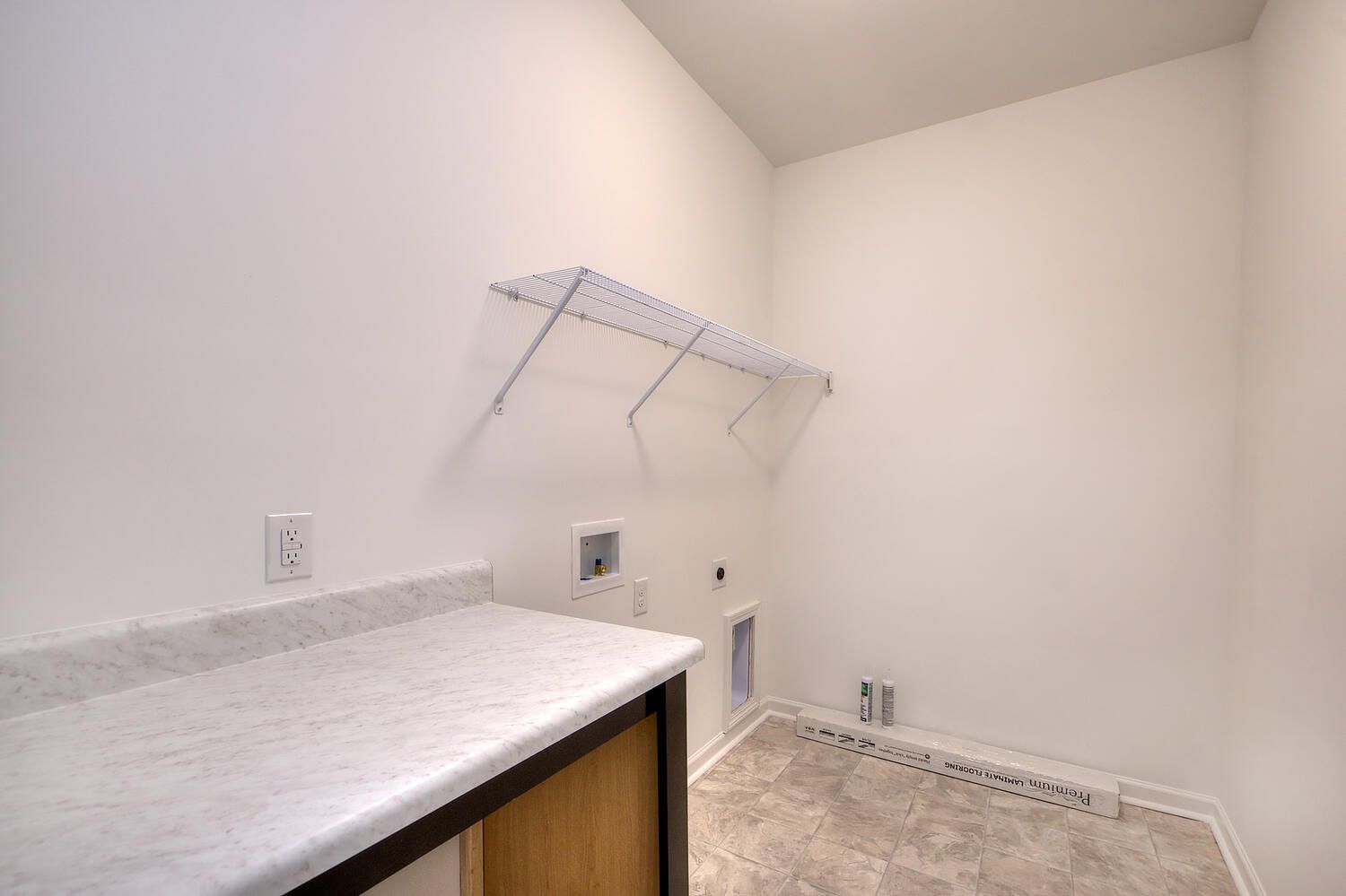 An empty laundry room with a counter and shelves.