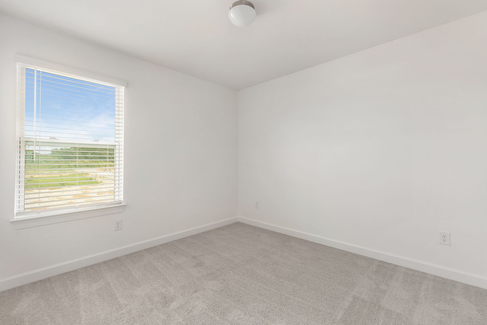 An empty bedroom with a window and blinds.