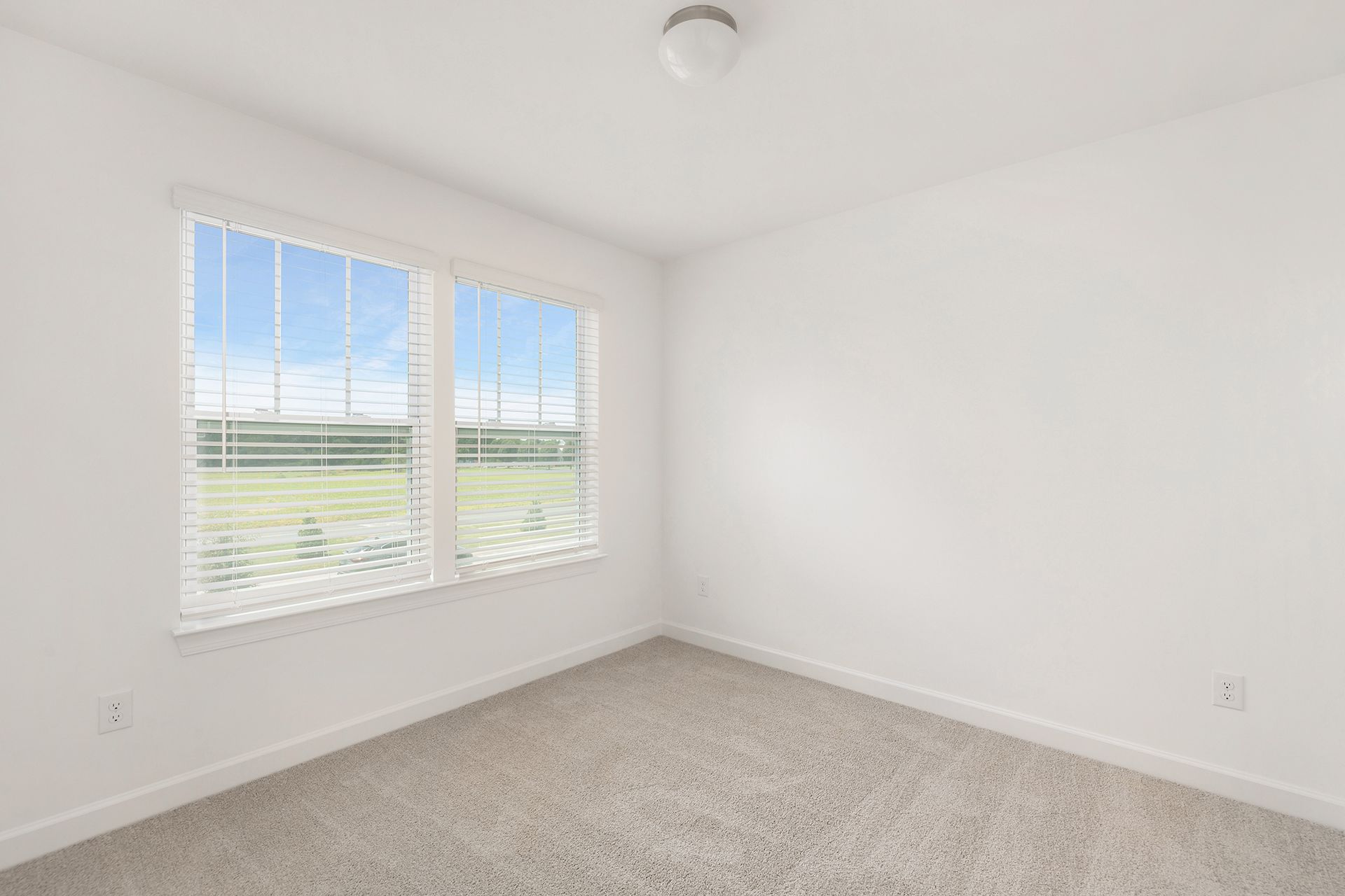 An empty bedroom with two windows and a carpeted floor.