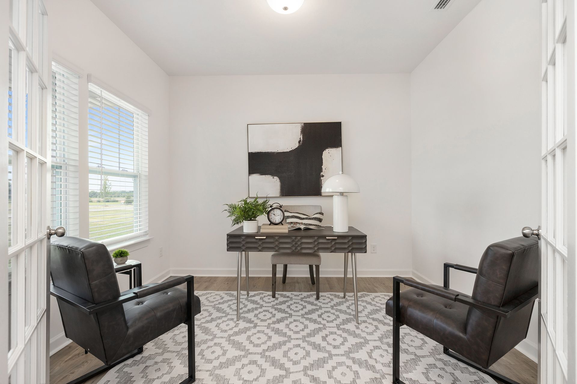 A home office with two chairs , a desk , and a painting on the wall.