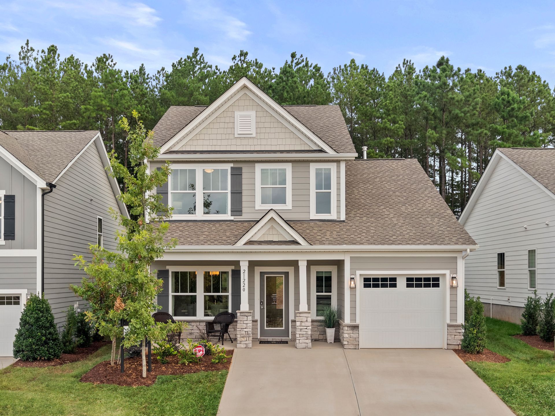 A large gray house with a white garage door is surrounded by trees.