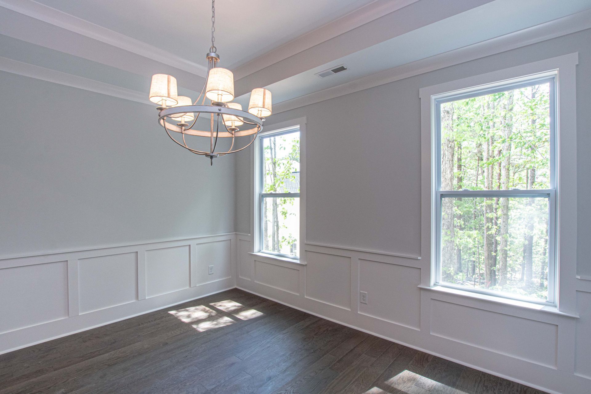 An empty dining room with a chandelier and lots of windows.