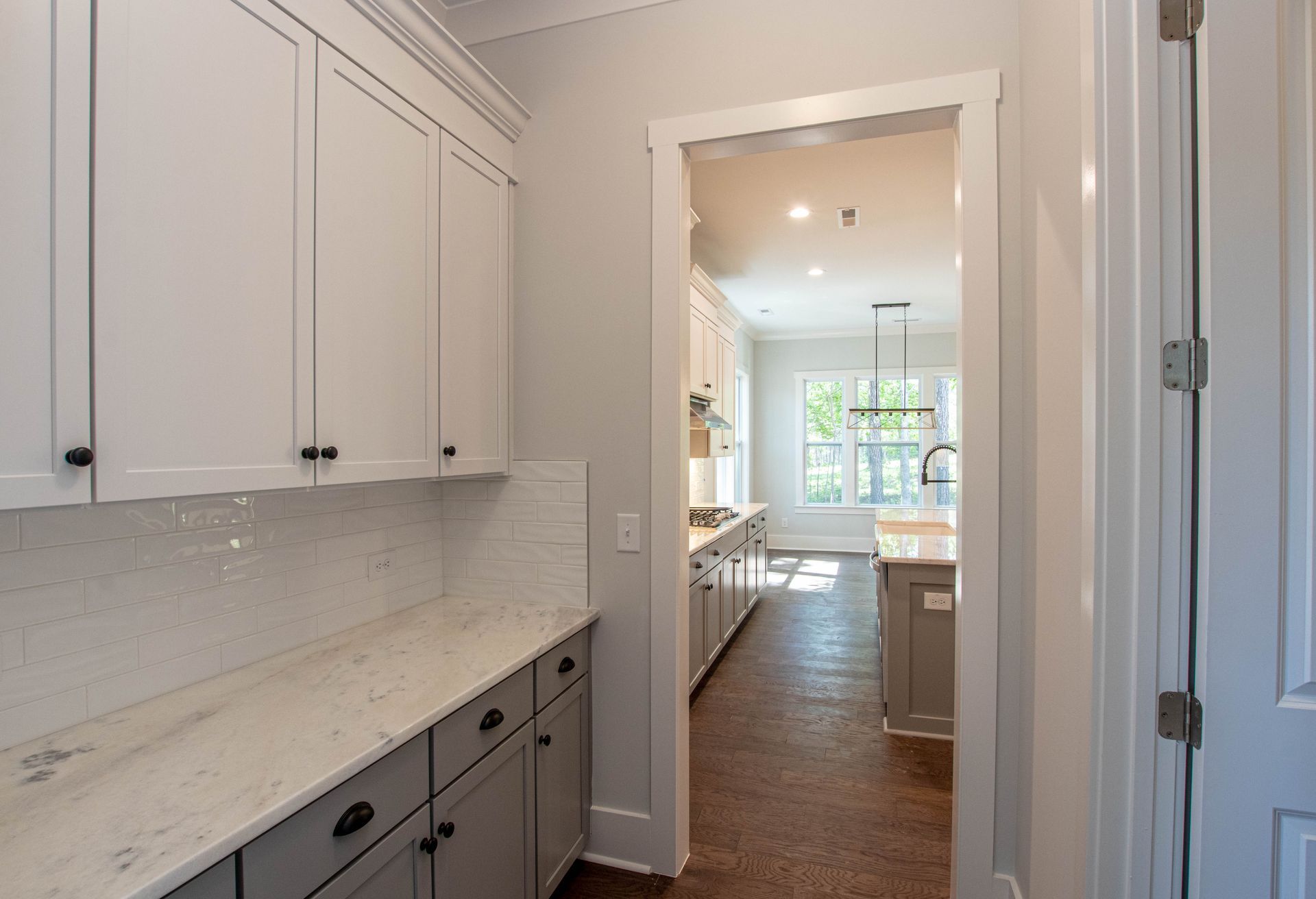 A kitchen with white cabinets and gray counter tops leading to a kitchen.