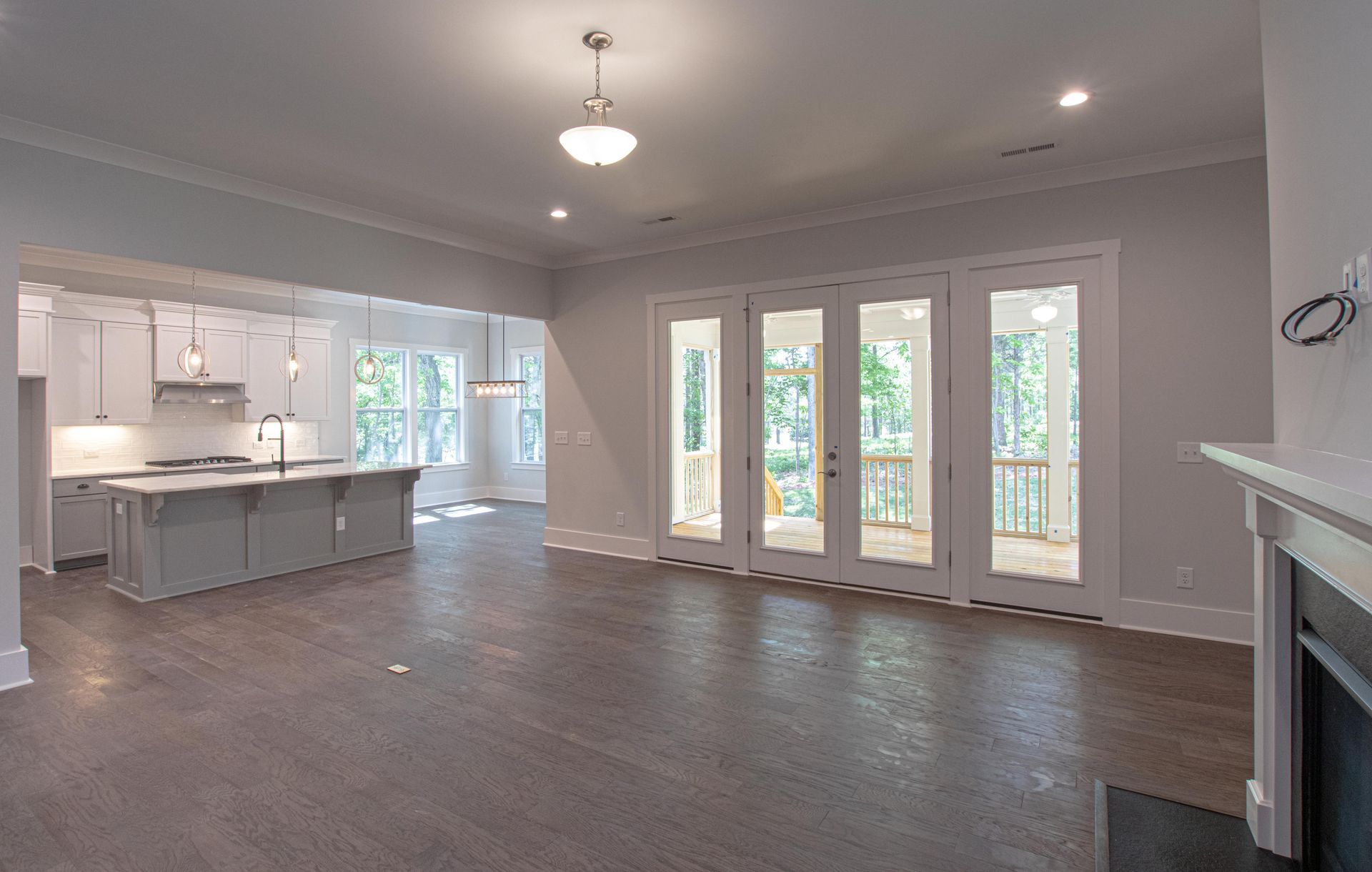 An empty living room with a fireplace and a kitchen in the background.