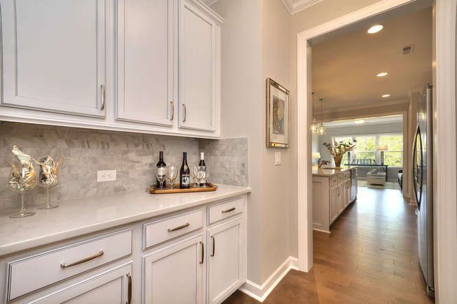 A kitchen with white cabinets and bottles of wine on the counter.