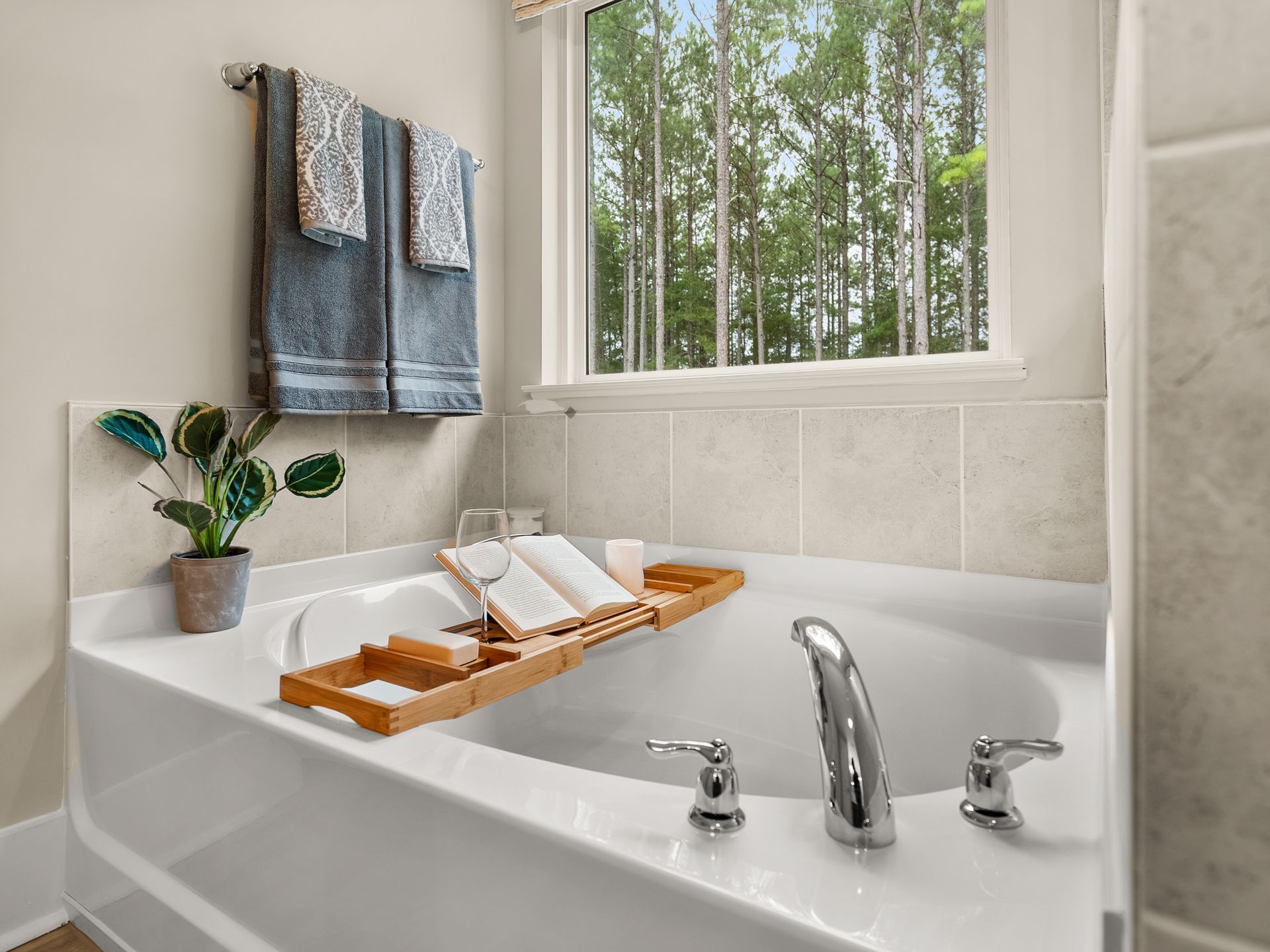 A bathtub with a book on a tray in a bathroom next to a window.
