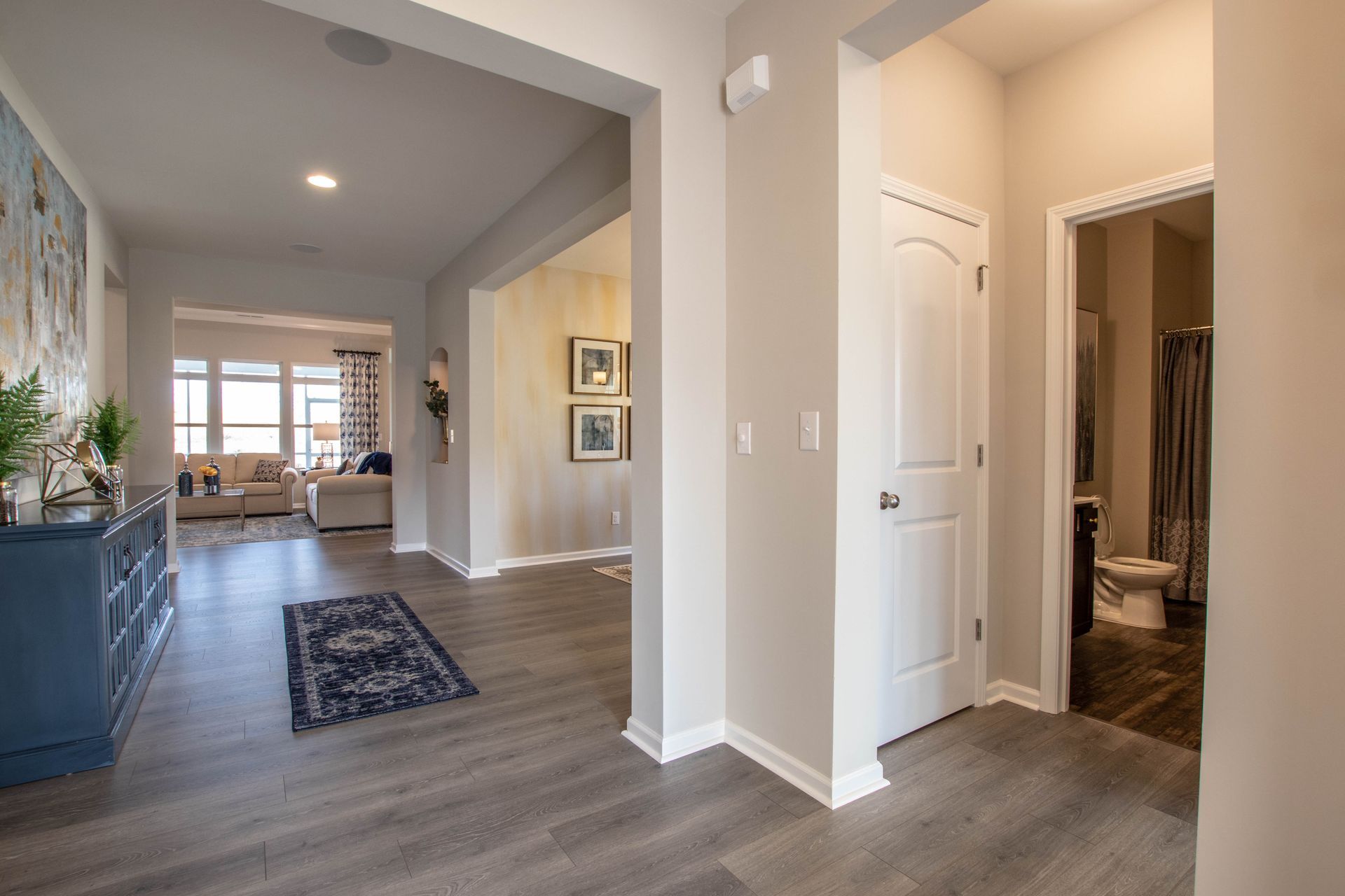 A hallway in a house with hardwood floors and a bathroom.