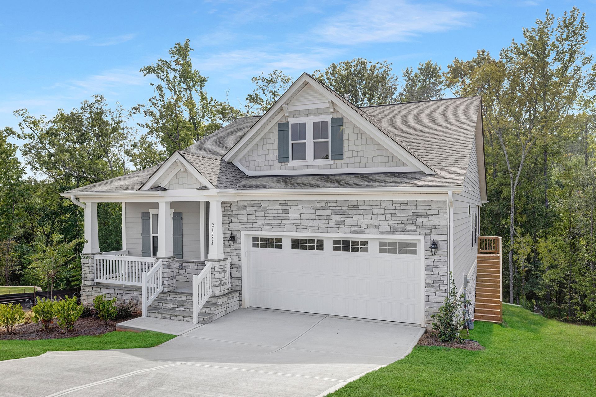 A white house with a large garage and a porch surrounded by trees.
