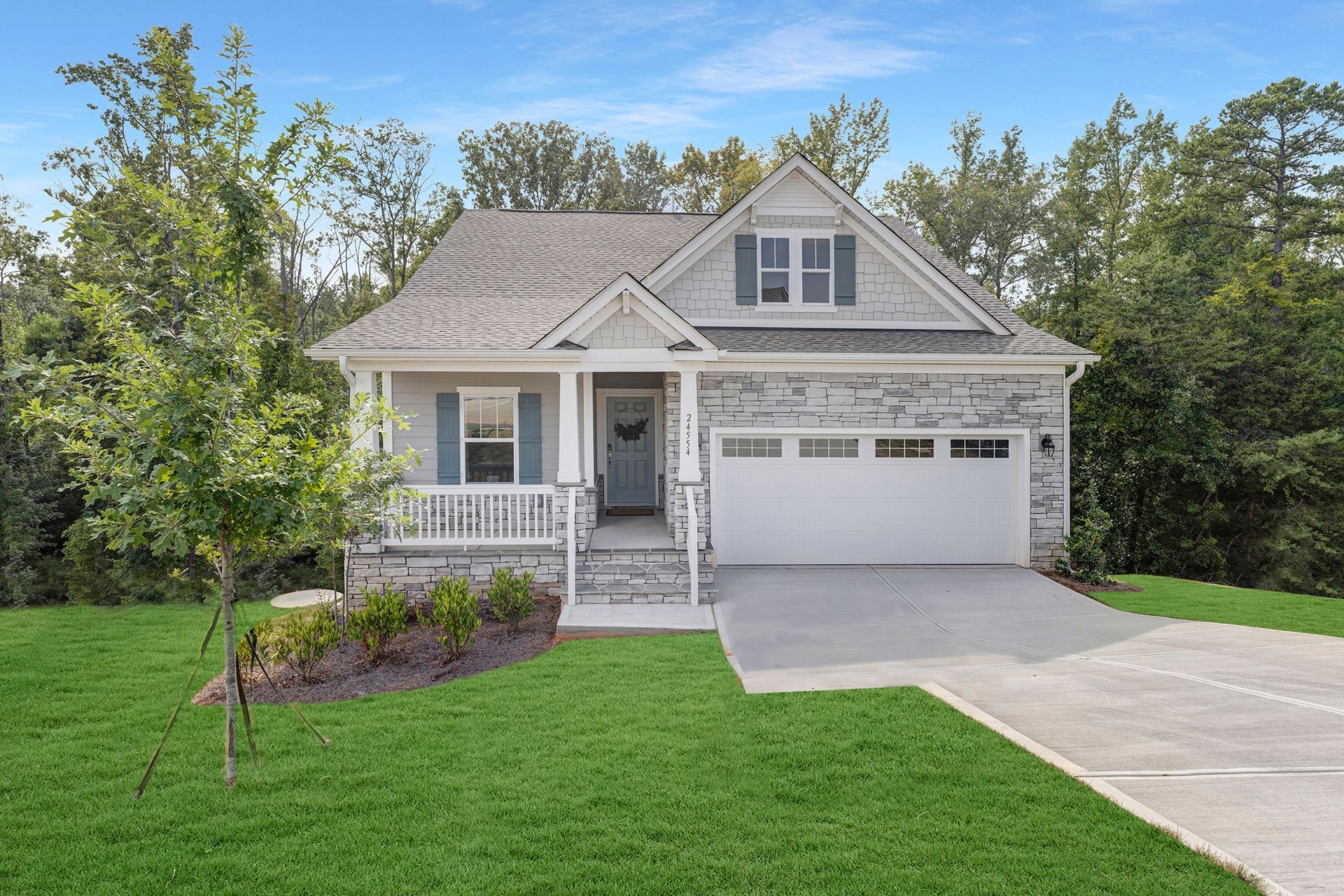 A house with a white garage door and a porch surrounded by trees.