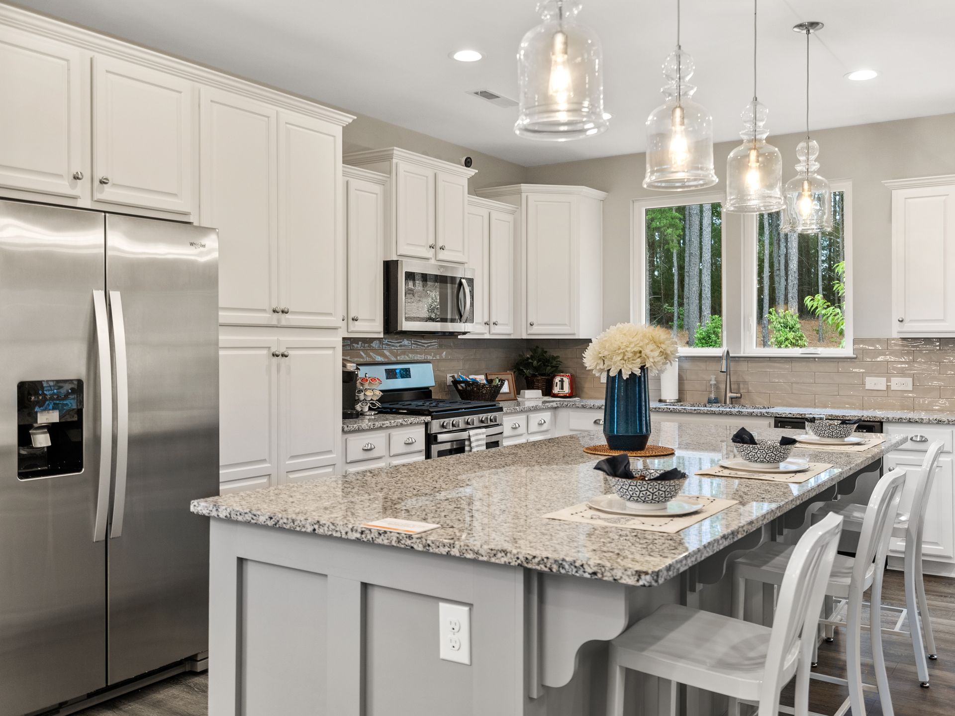 A kitchen with white cabinets , granite counter tops , stainless steel appliances and a large island.