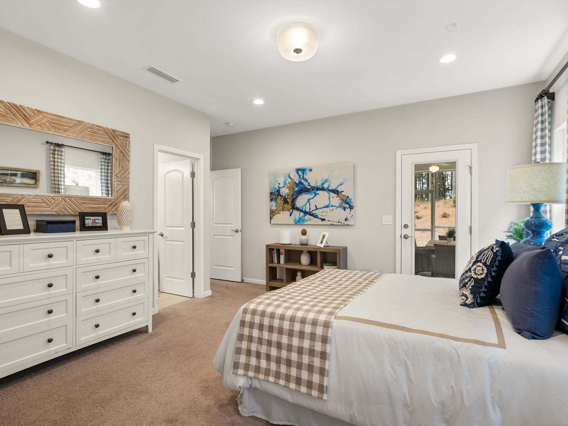 A bedroom with a bed , dresser , mirror and painting on the wall.
