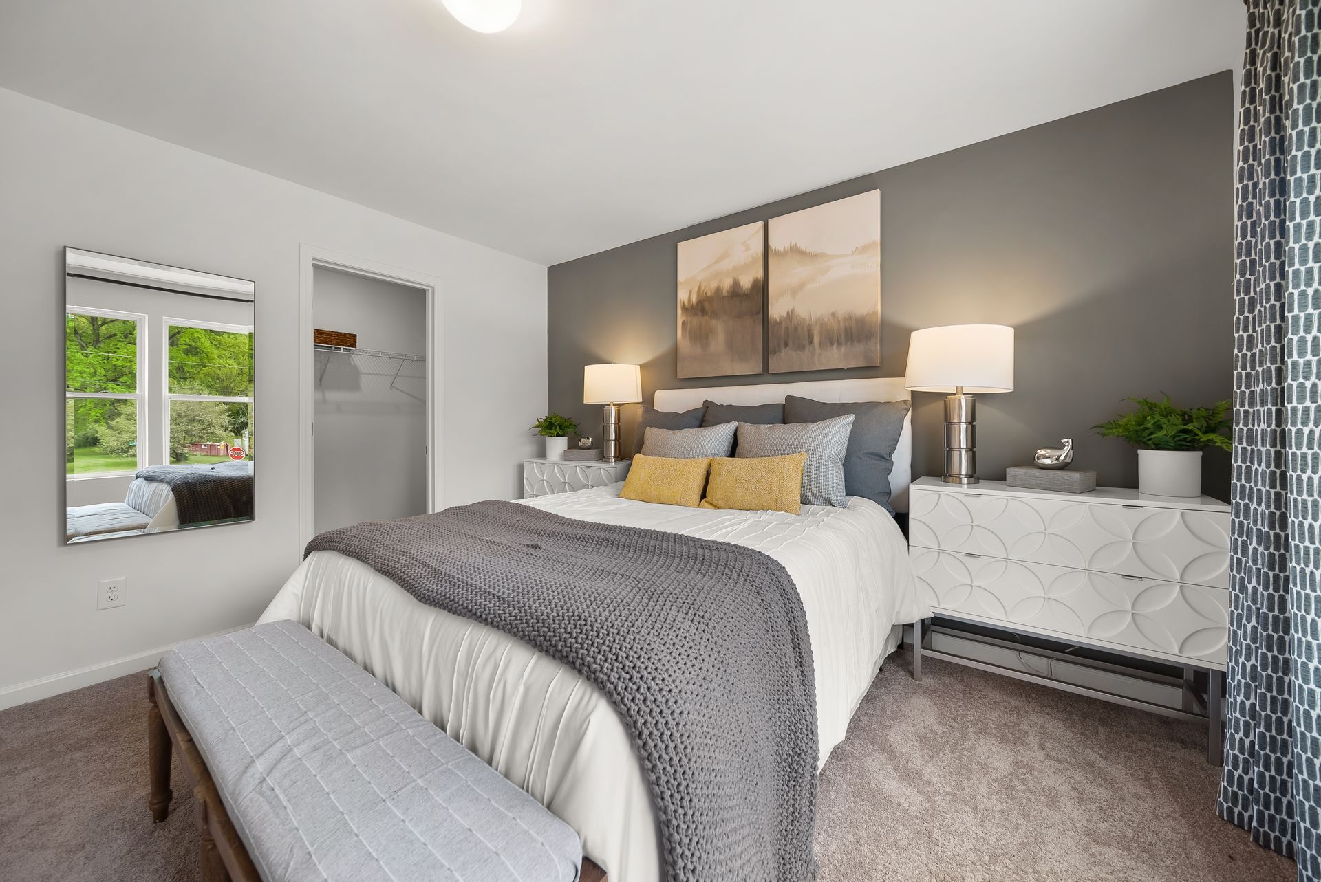 A bedroom with a bed , nightstand , mirror and bench.