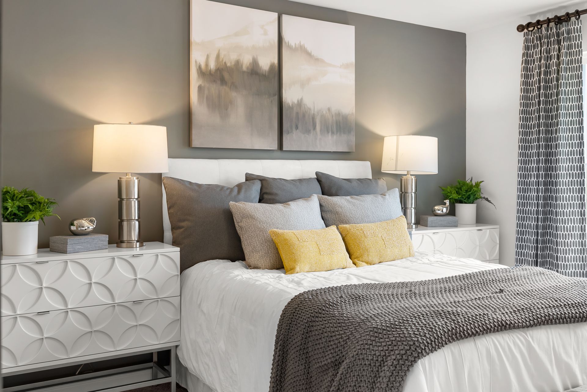 A bedroom with a bed , nightstand , lamps and paintings on the wall.