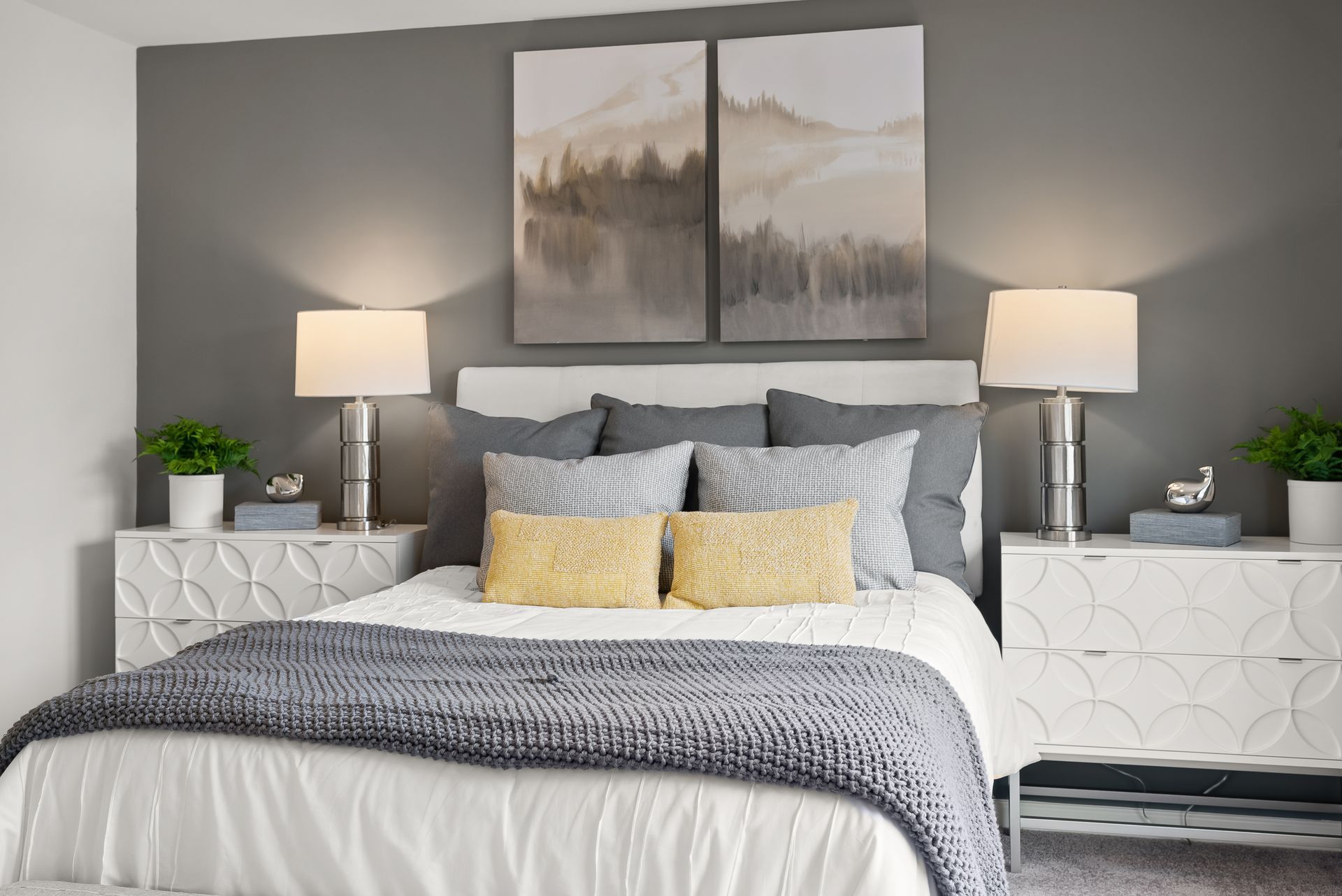 A bedroom with a bed , nightstands , lamps and paintings on the wall.