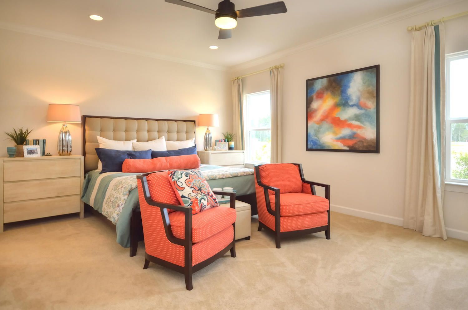 A bedroom with a bed , two chairs , a dresser and a ceiling fan.