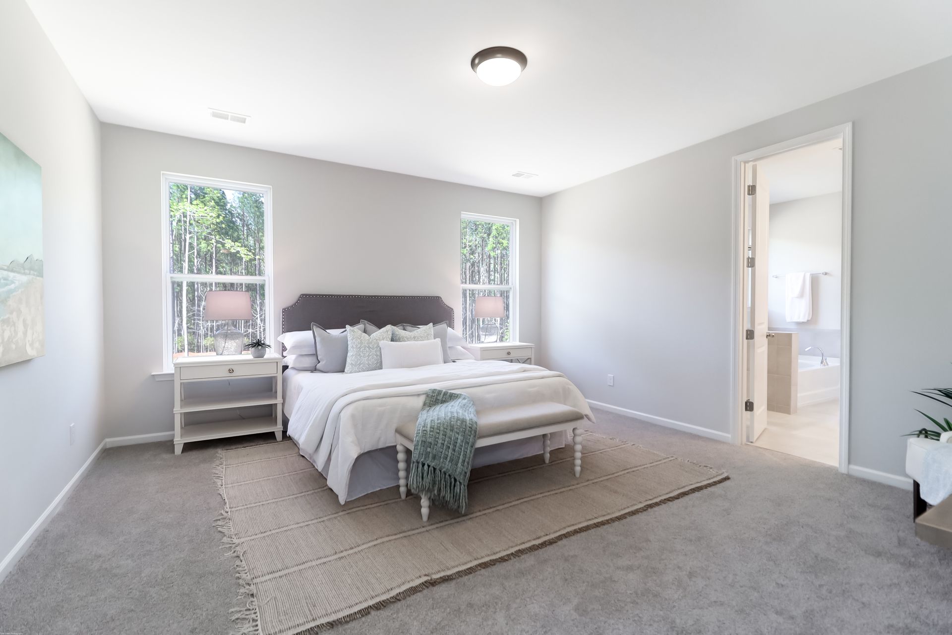 A bedroom with a large bed , two windows , a bench and a rug.