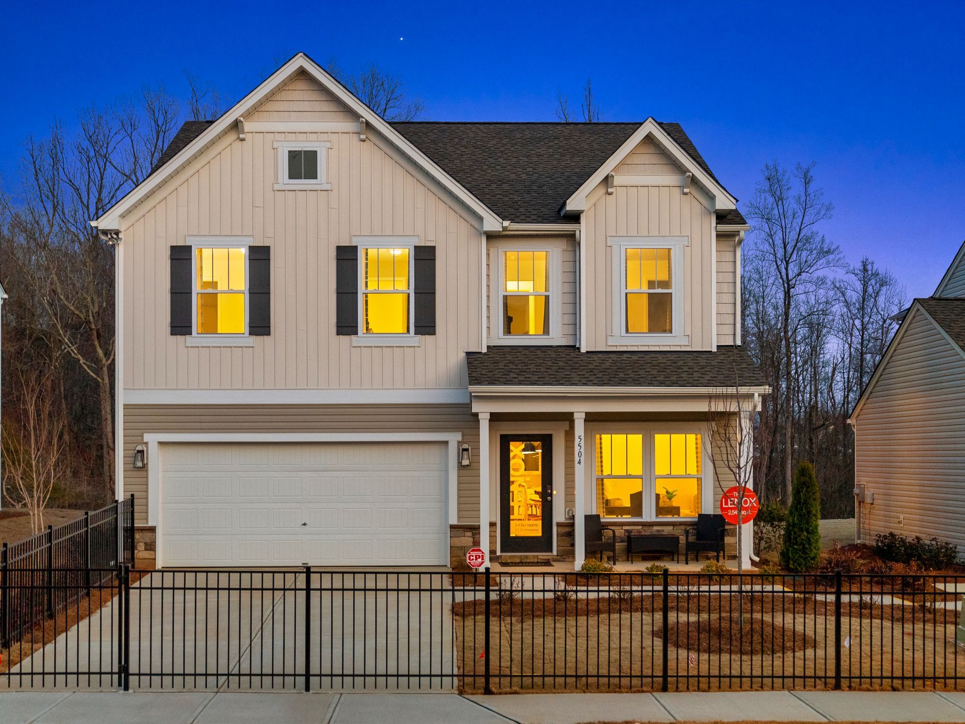 The front of a house with a fence and a garage is lit up at night.