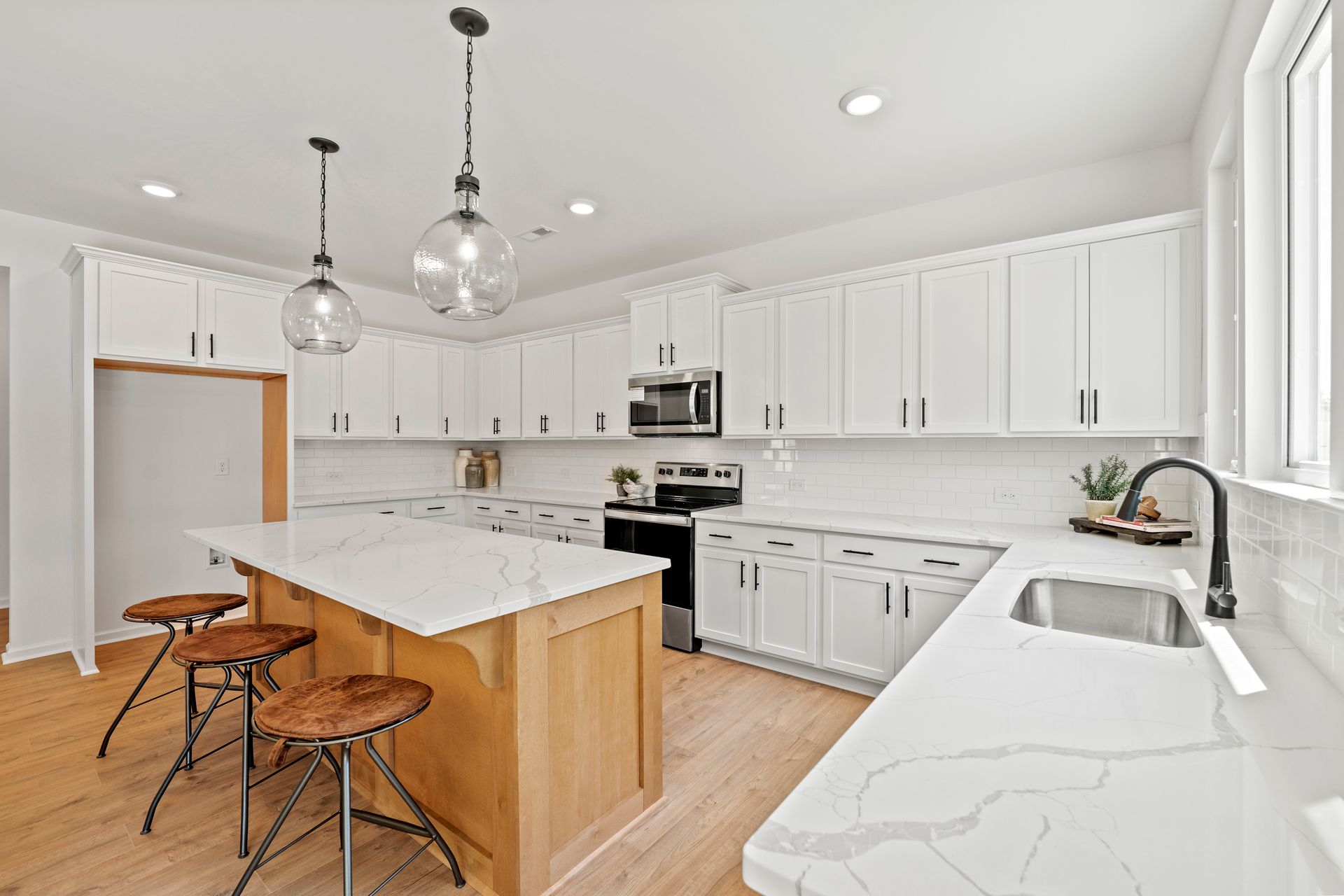 A kitchen with white cabinets , a large island , a sink , and a microwave.