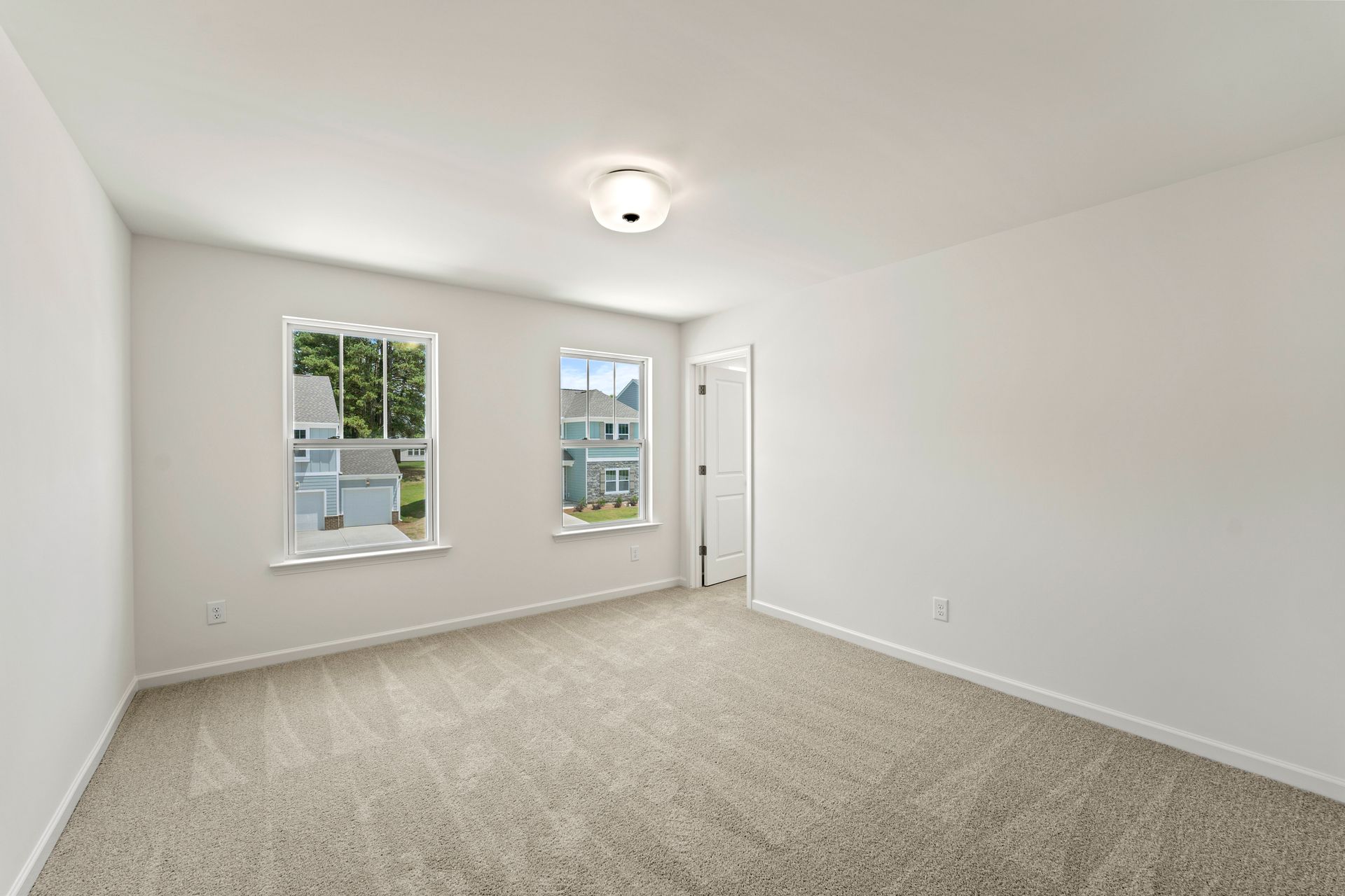 An empty bedroom with a carpeted floor and two windows.