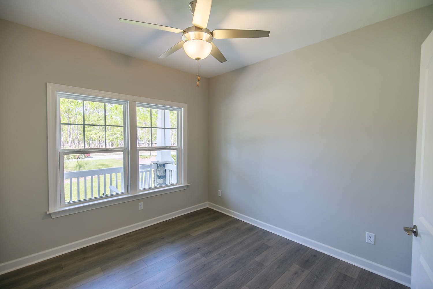 An empty room with a ceiling fan and two windows.