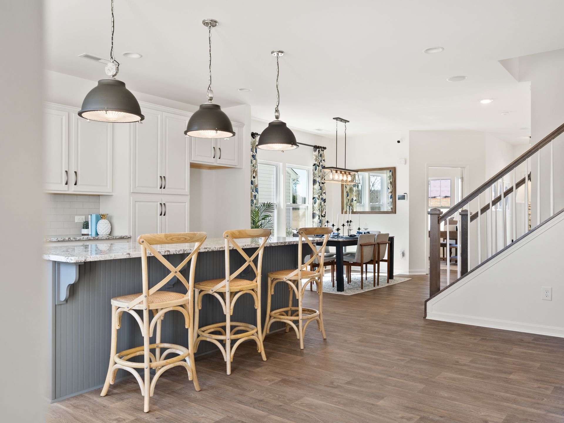 A kitchen with a large island and stools and a staircase leading to the dining room.