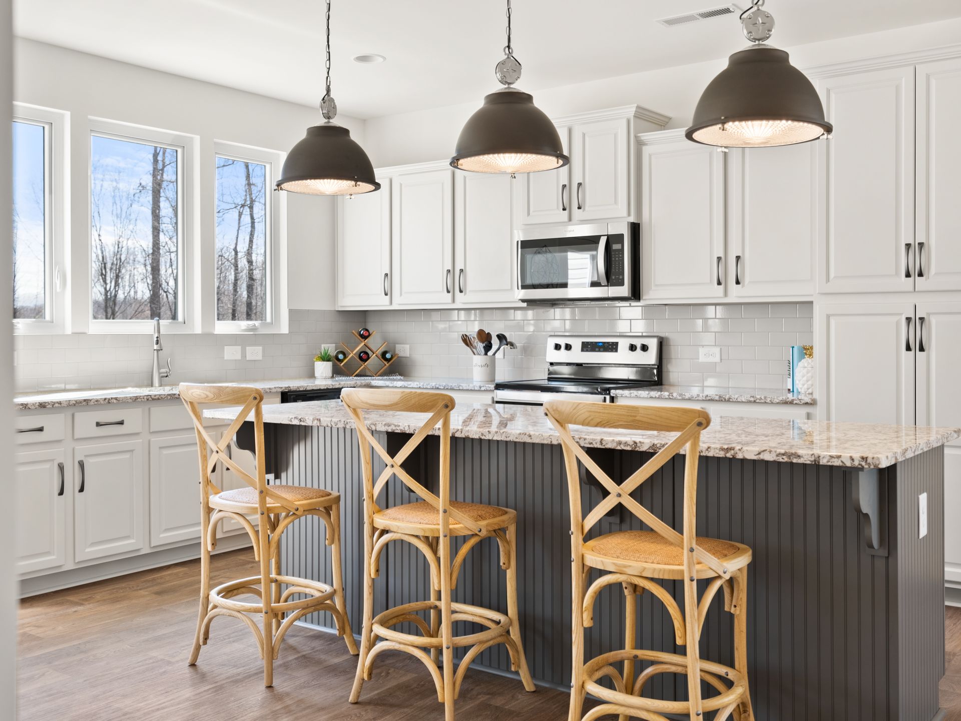 A kitchen with white cabinets , a large island , stools and a stove.